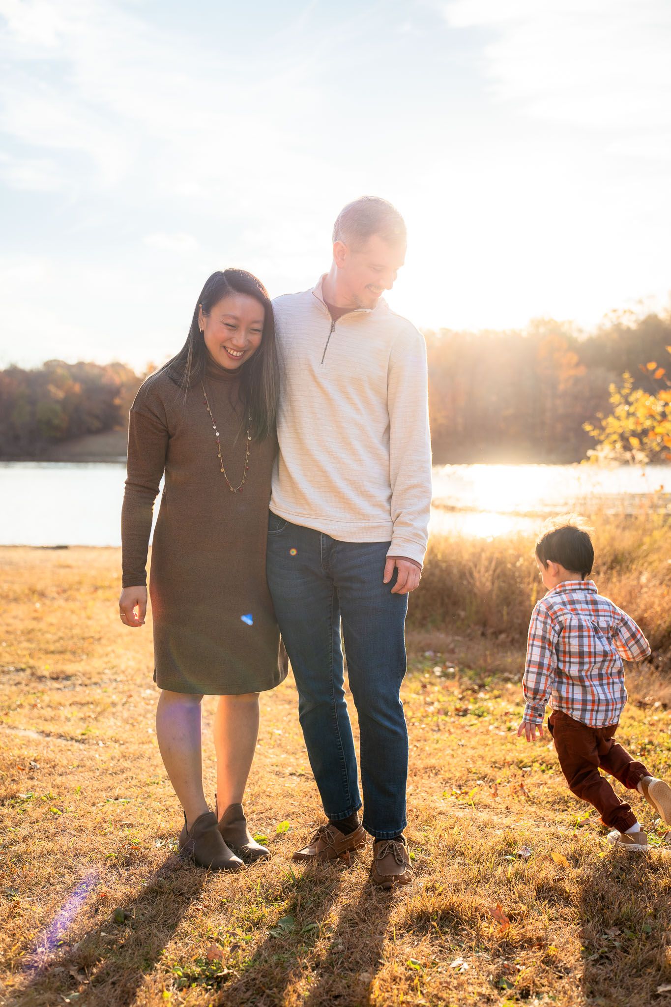 Family walking together in a golden field at sunset casting long shadows on the grass.