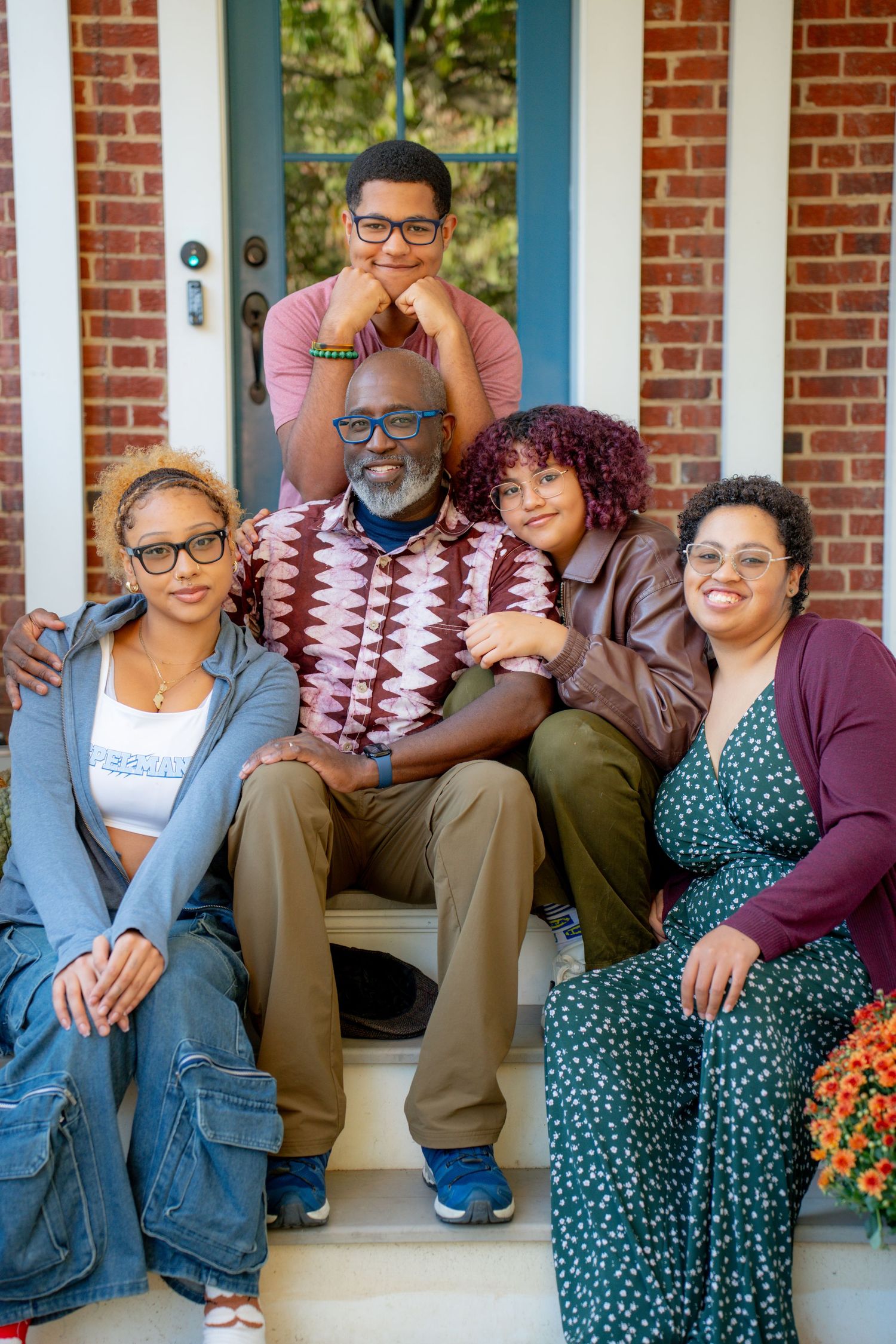 A family group sits together on brick porch steps during a casual outdoor photo session.