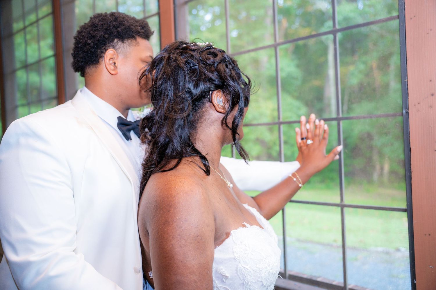 Couple sharing intimate moment by large windows during wedding celebration.