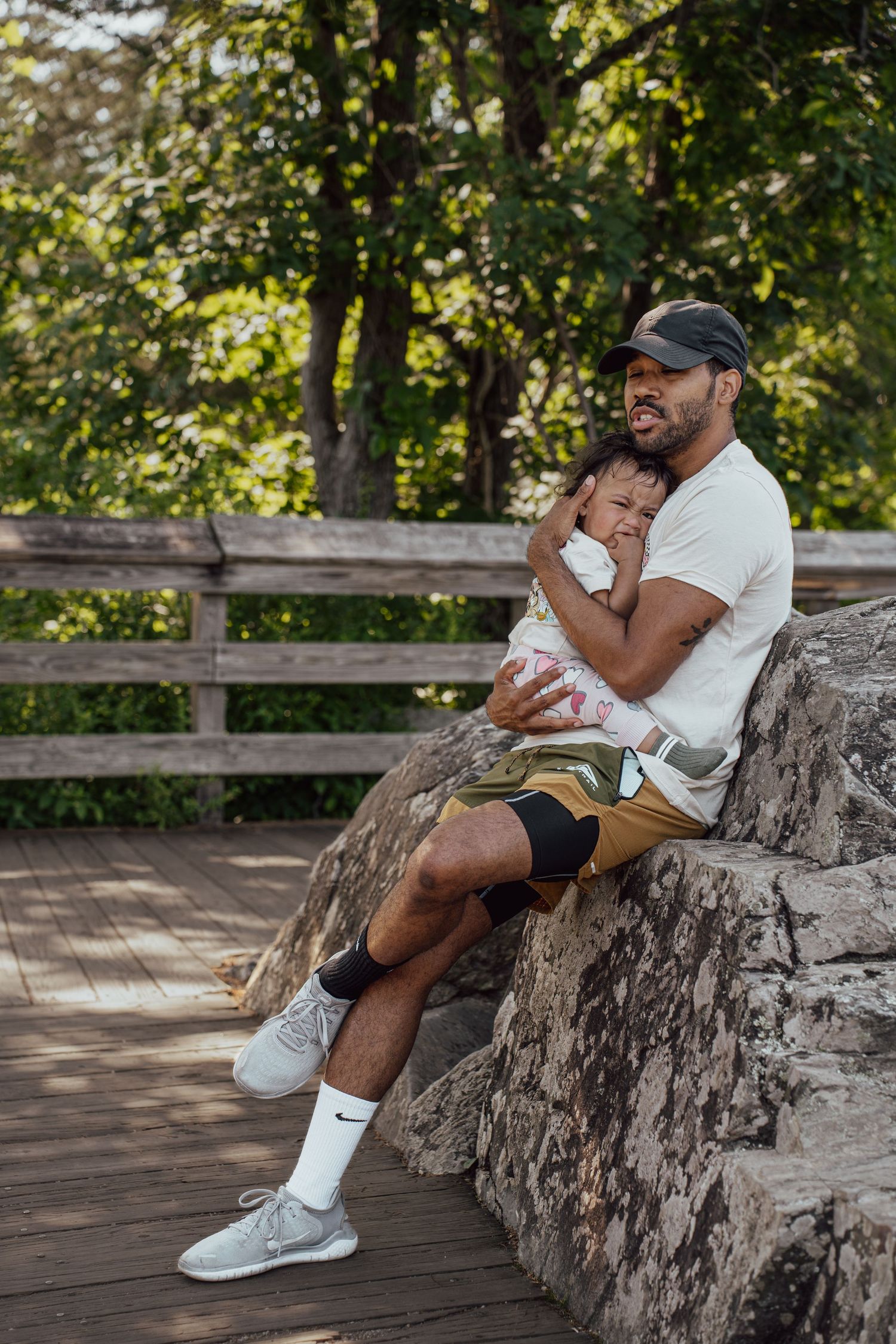 Two people sitting on a stone wall surrounded by greenery on a sunny day.