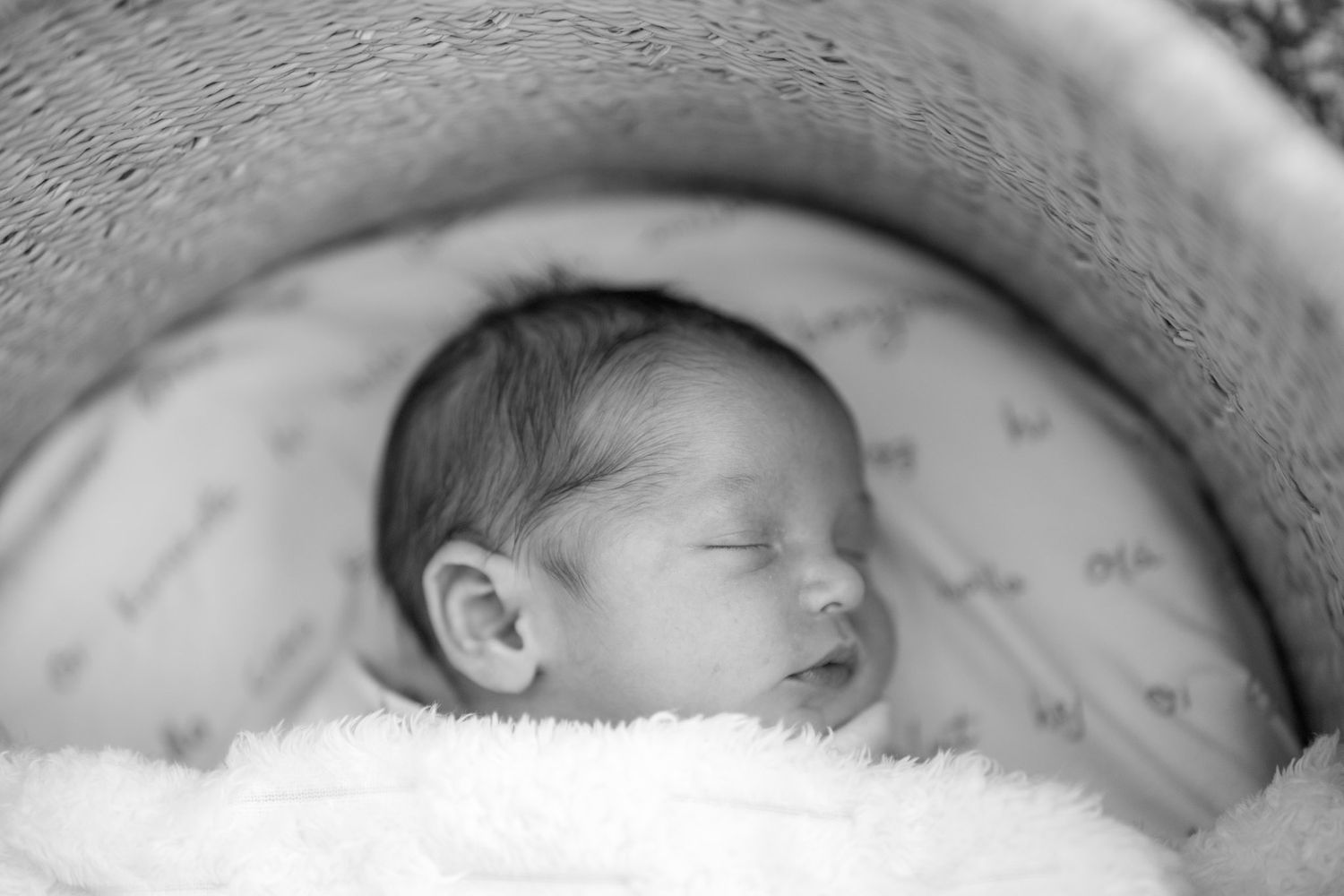 A peaceful sleeping newborn baby wrapped in soft blankets, captured in black and white photography.