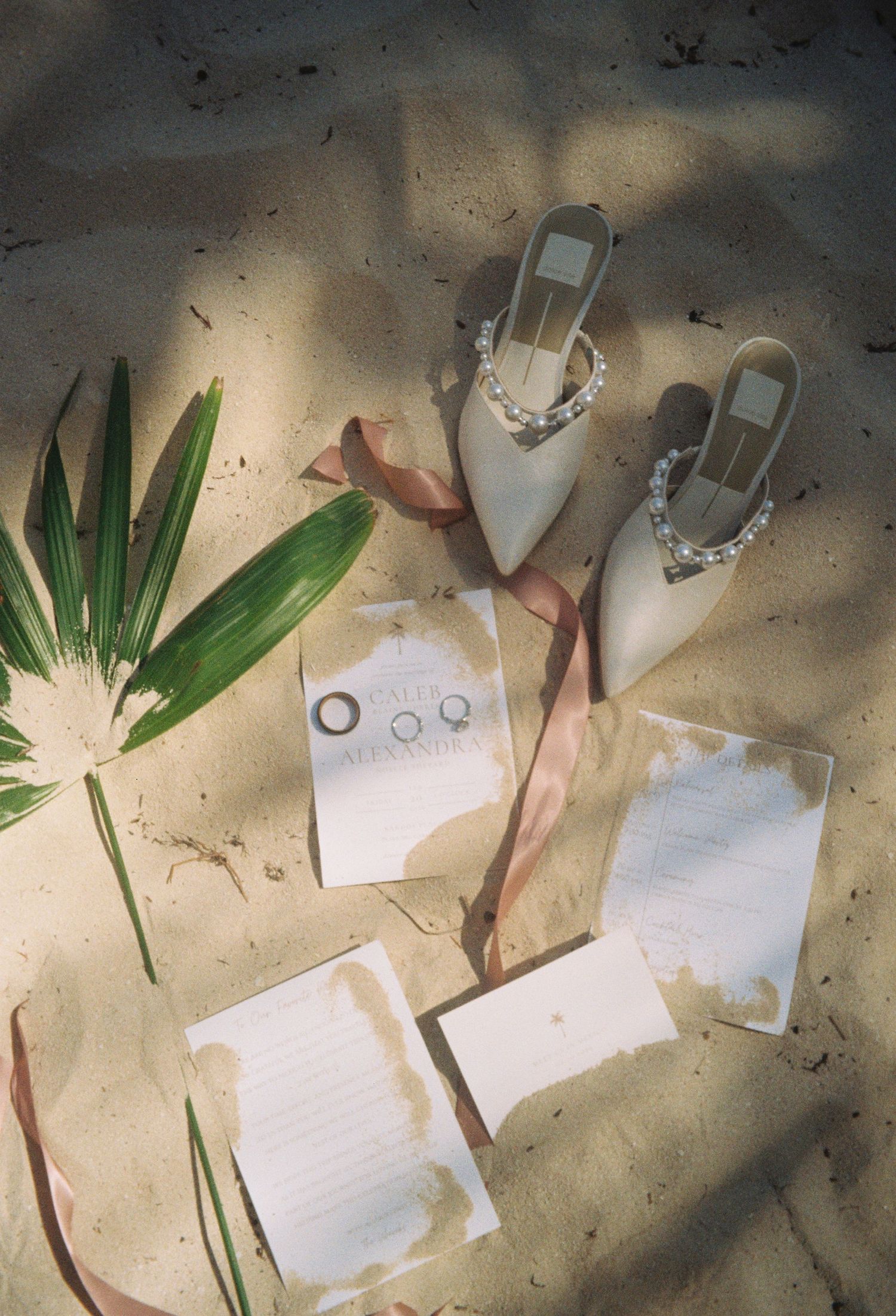 Wedding rings and palm leaves arranged artistically on a light surface with scattered papers and decorative elements.
