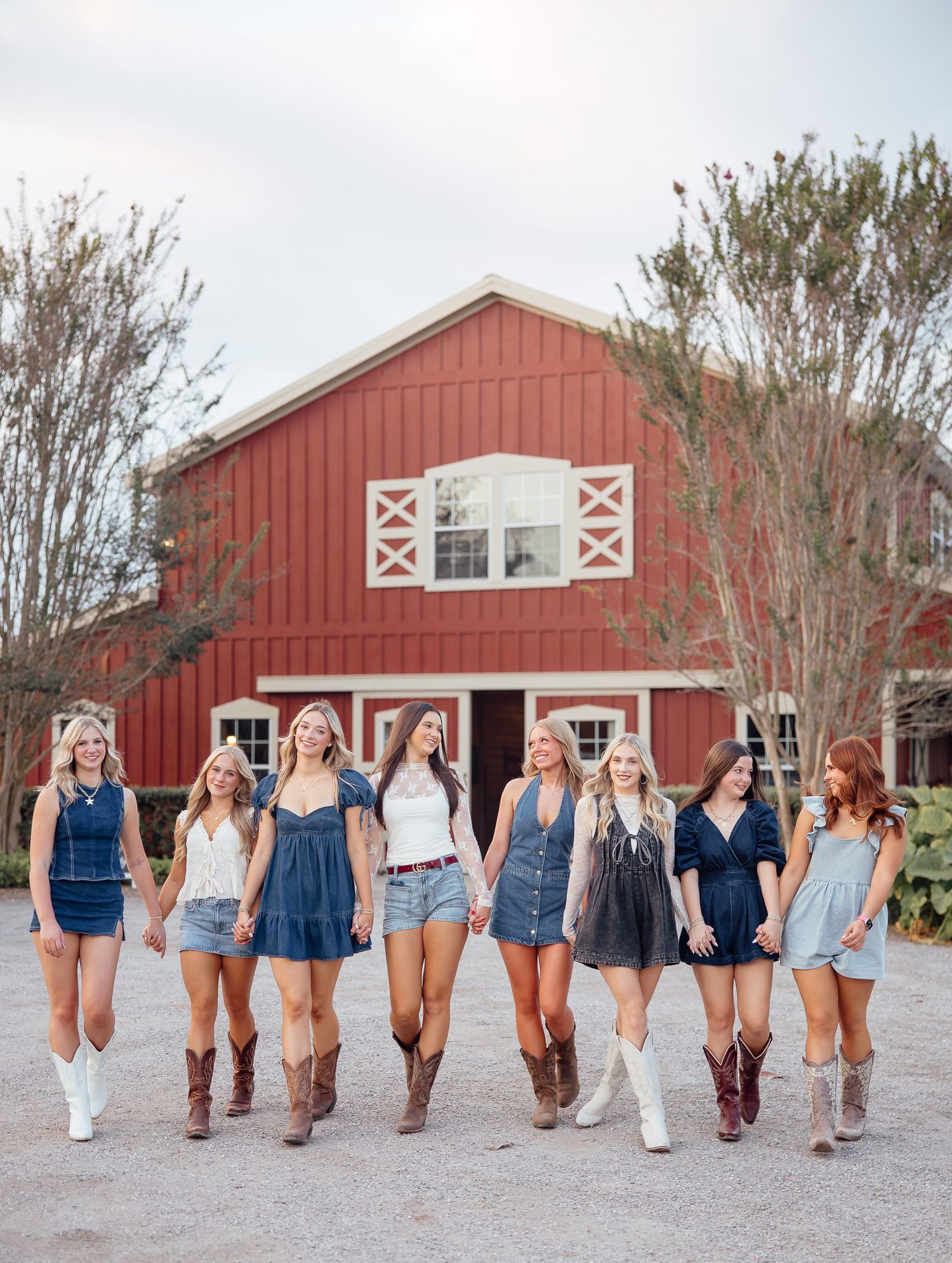 A line of people wearing denim shorts and navy tops pose facing away from camera in front of a red barn.
