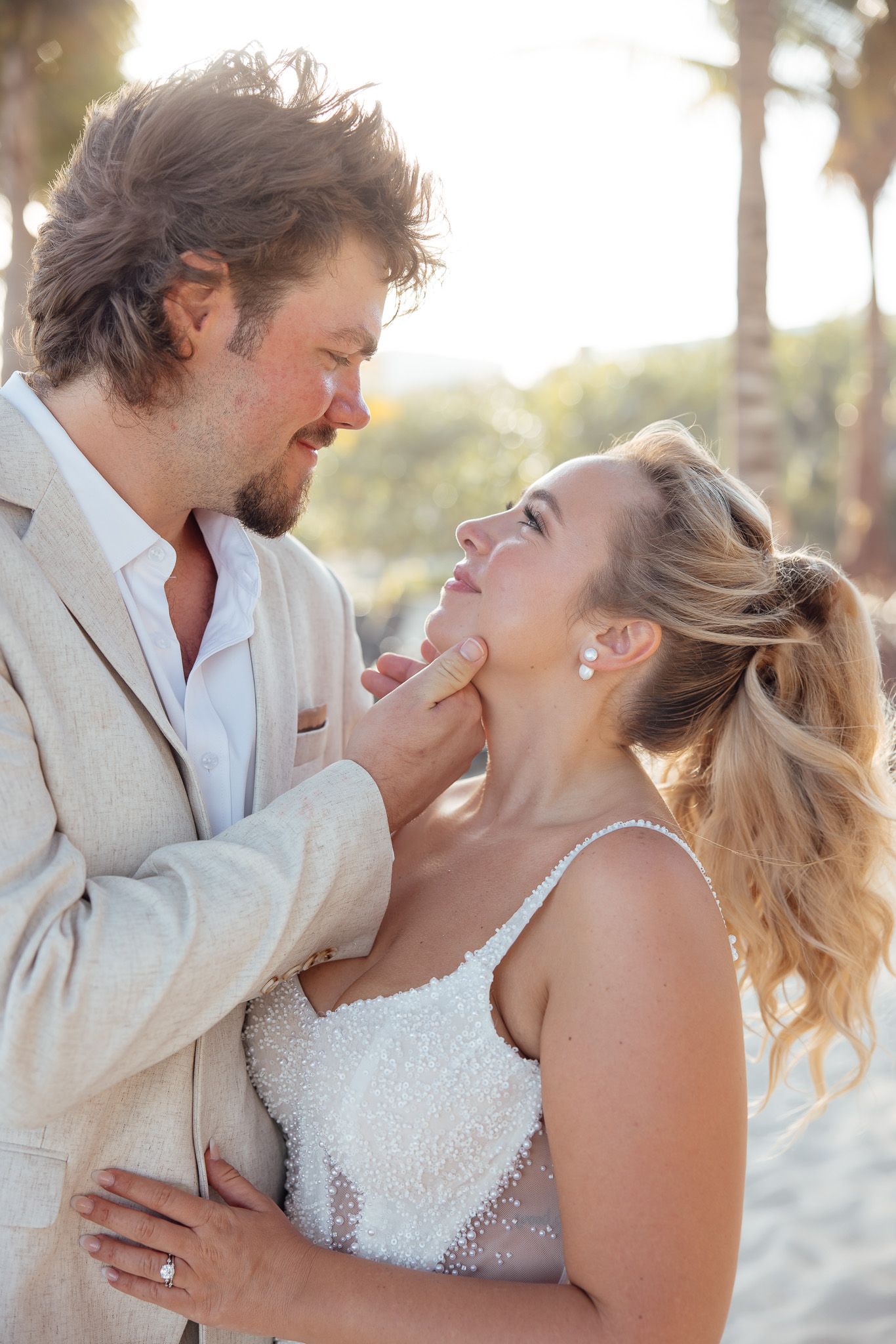A couple shares joyful laughter together on a sunny beach with palm trees in the background.