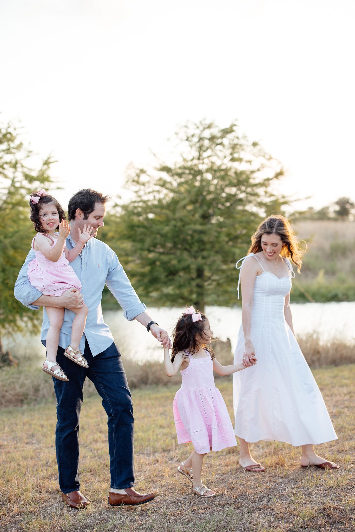 A family in coordinated outfits enjoys a golden hour outdoor photo session in a grassy field at sunset.