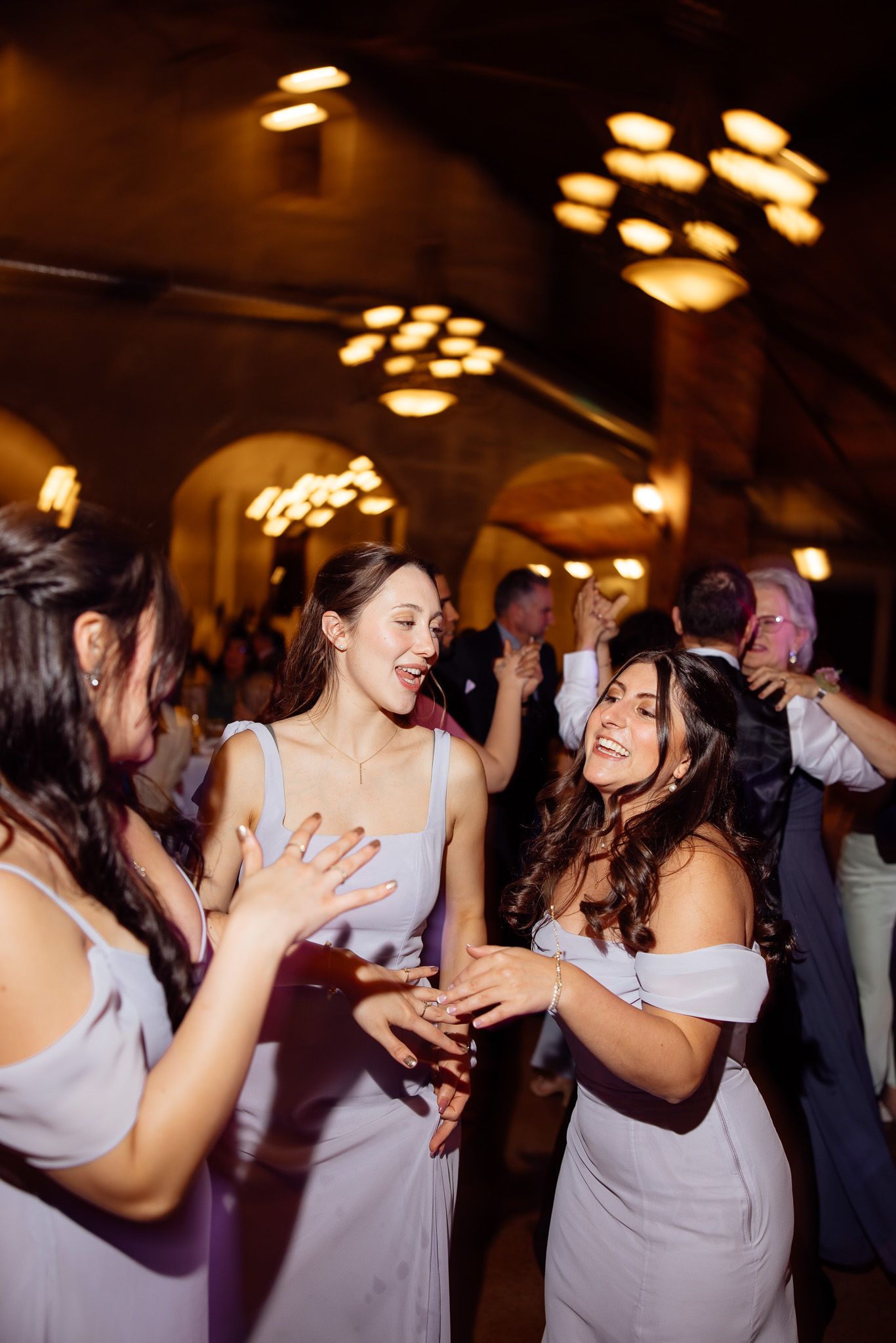Bridesmaids in lavender dresses dancing joyfully at a wedding reception with warm ambient lighting.