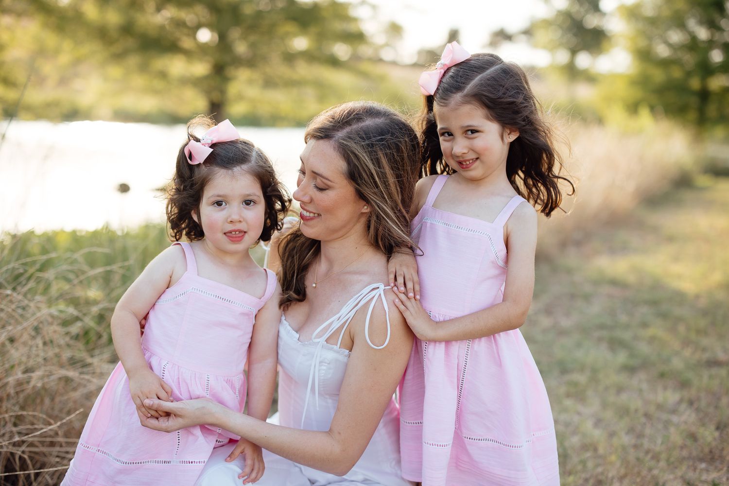 A tender family moment outdoors in matching pink dresses against a sunlit natural background.