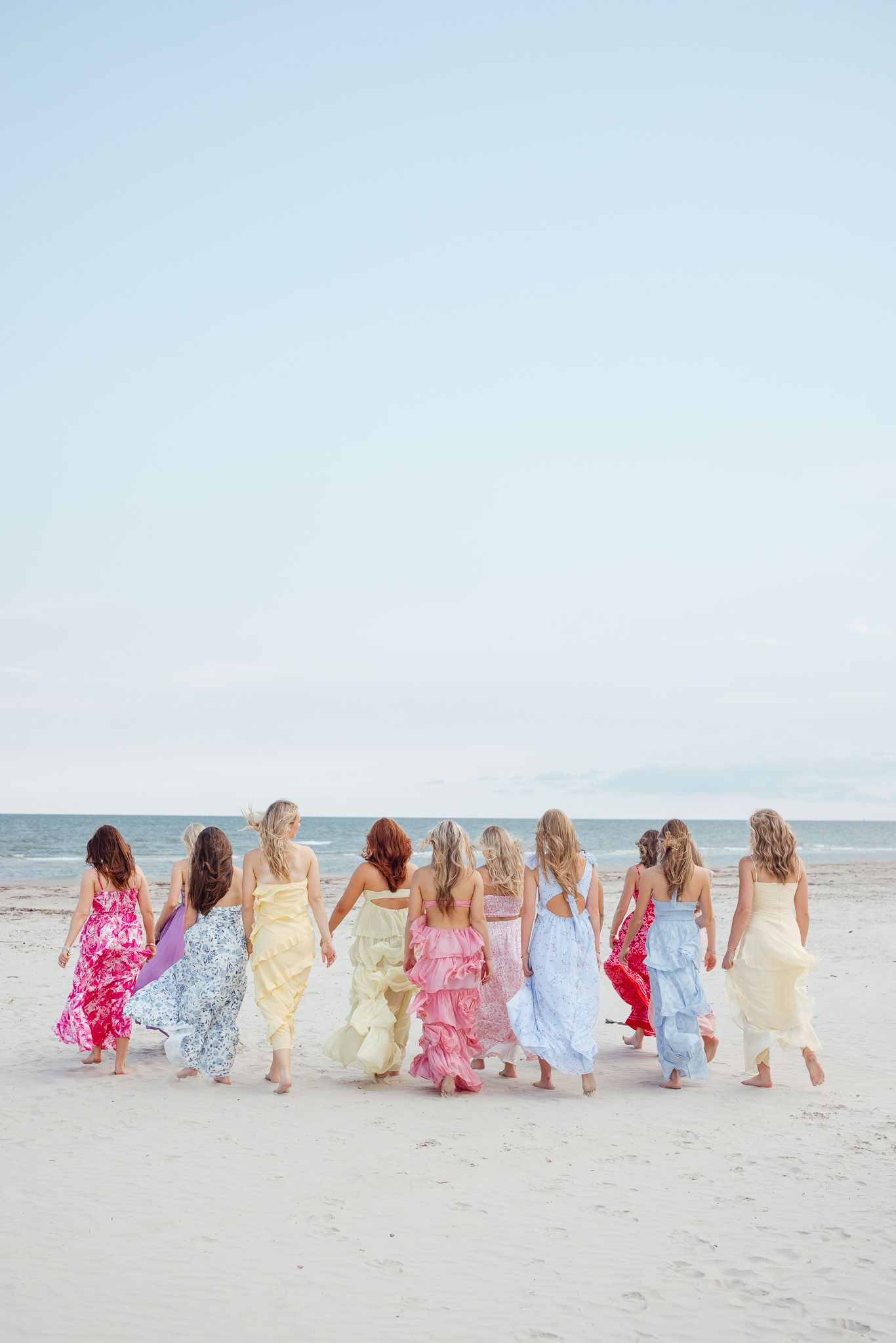 A group in colorful sundresses sits together on a sandy beach looking out at the ocean horizon.