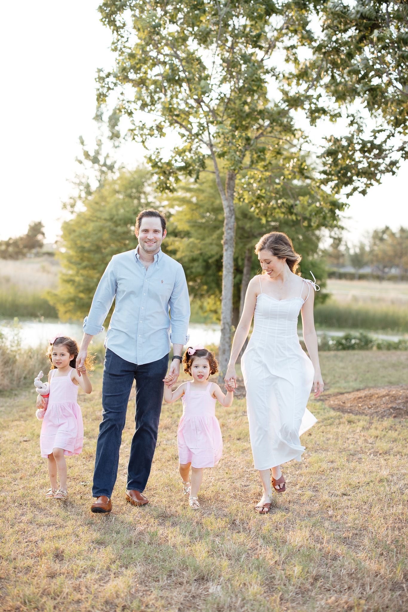 Family walking together holding hands in a sunny field during sunset.