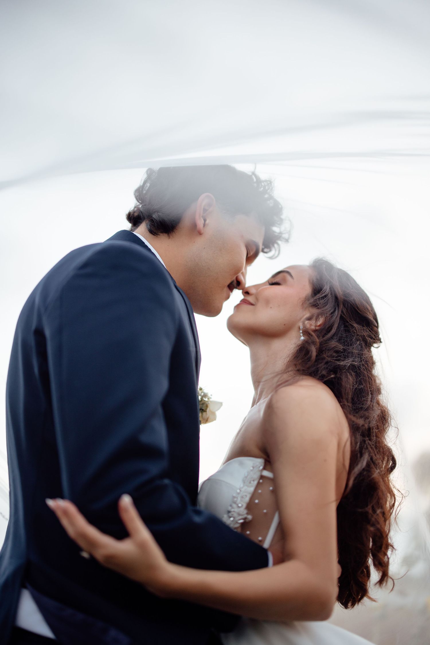 Romantic moment between newlyweds sharing a kiss under a white veil.