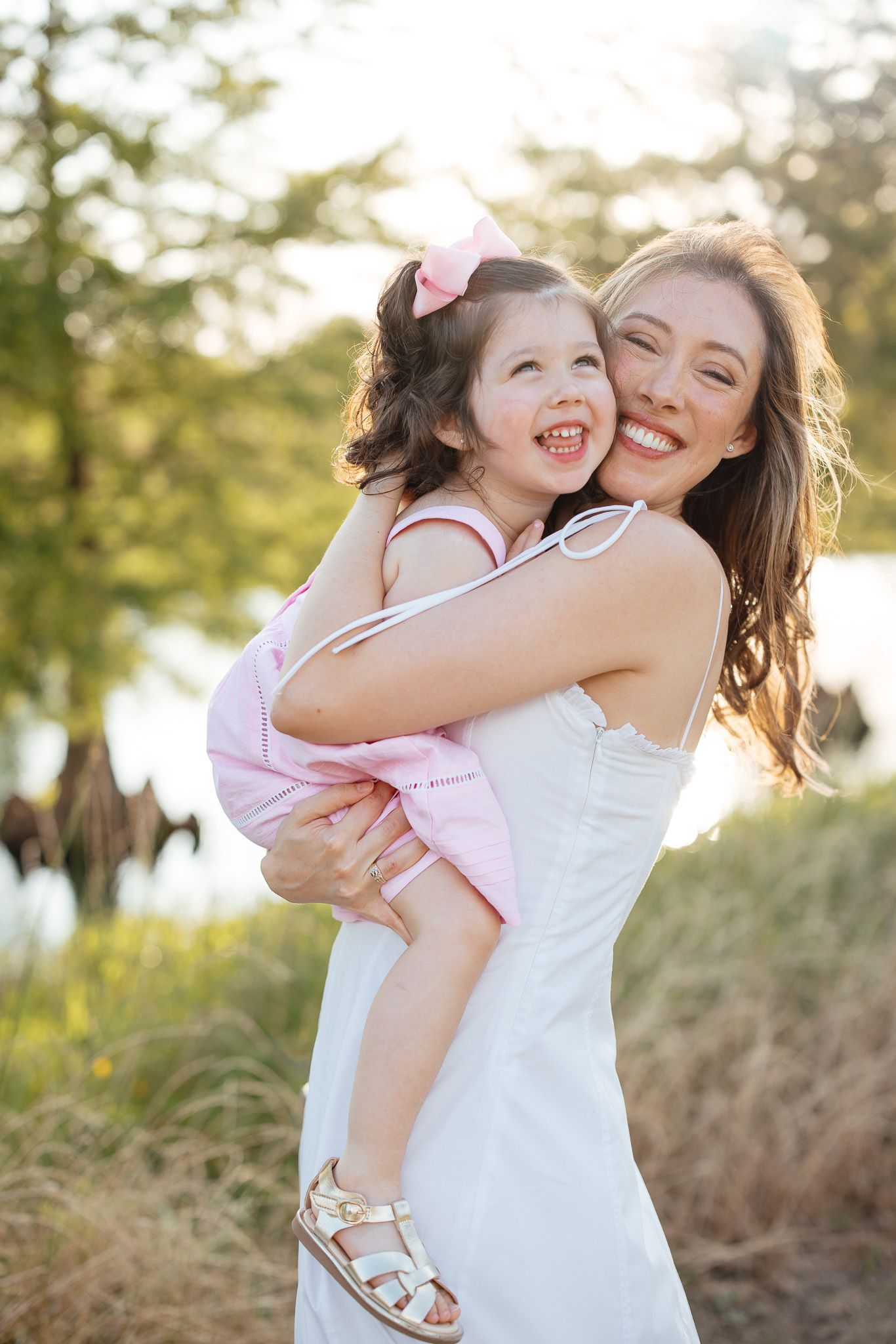 Mother and daughter share joyful embraces and laughter in sunlit field with warm golden hour lighting.