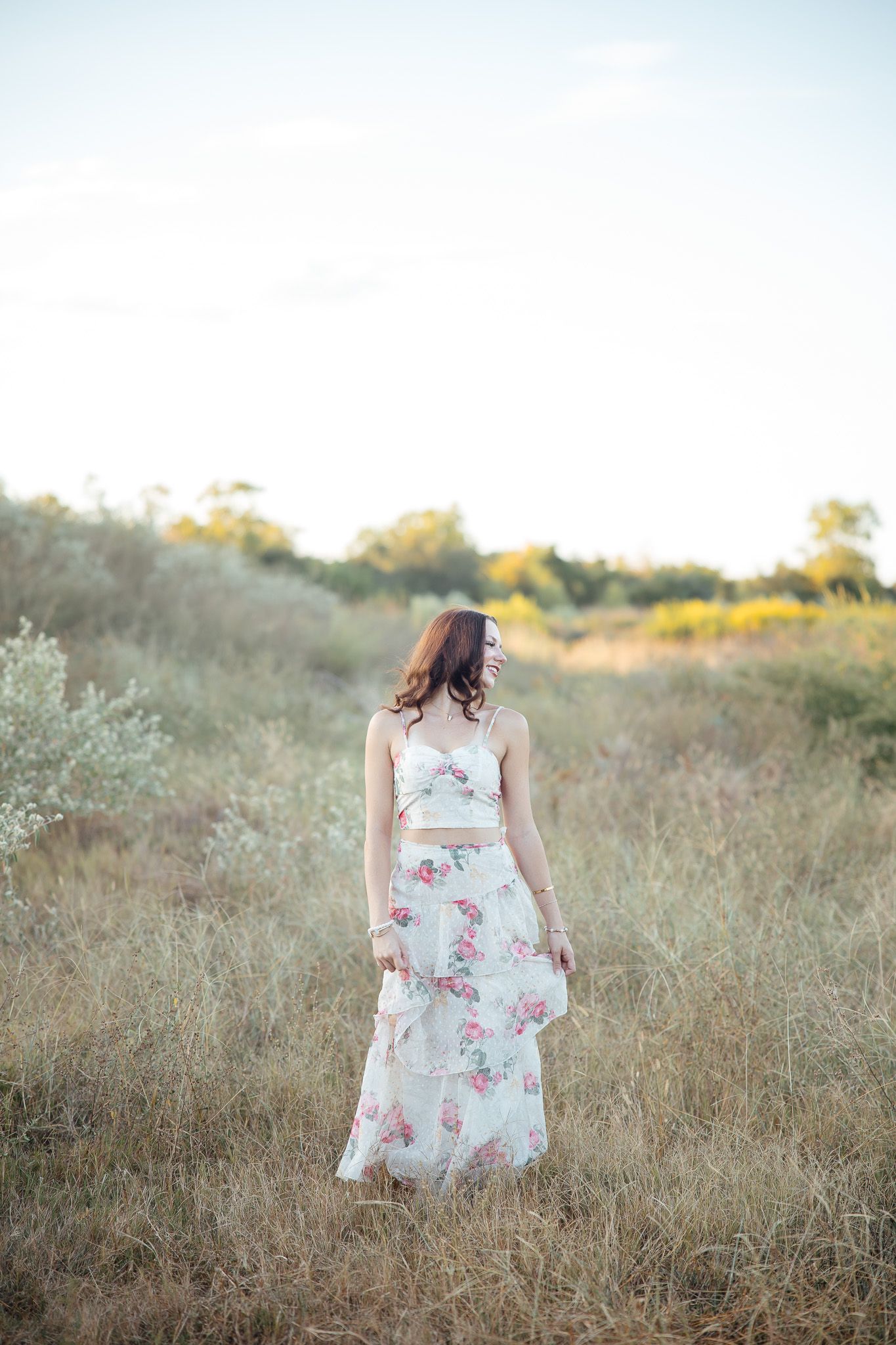 A person wearing a white floral dress stands in a golden field during sunset.