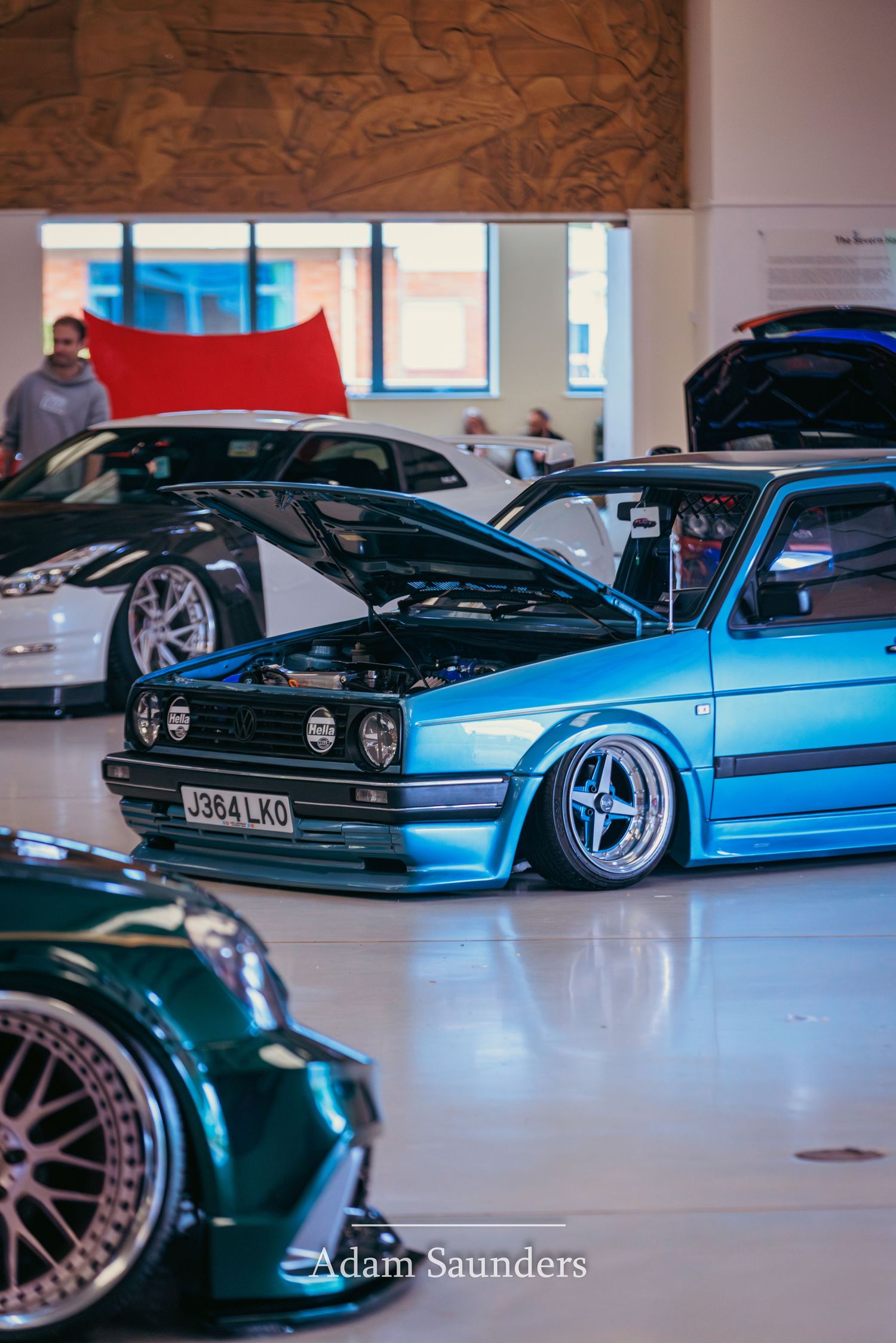 Modified blue Volkswagen Golf with lowered suspension and custom wheels displayed at an indoor car show.