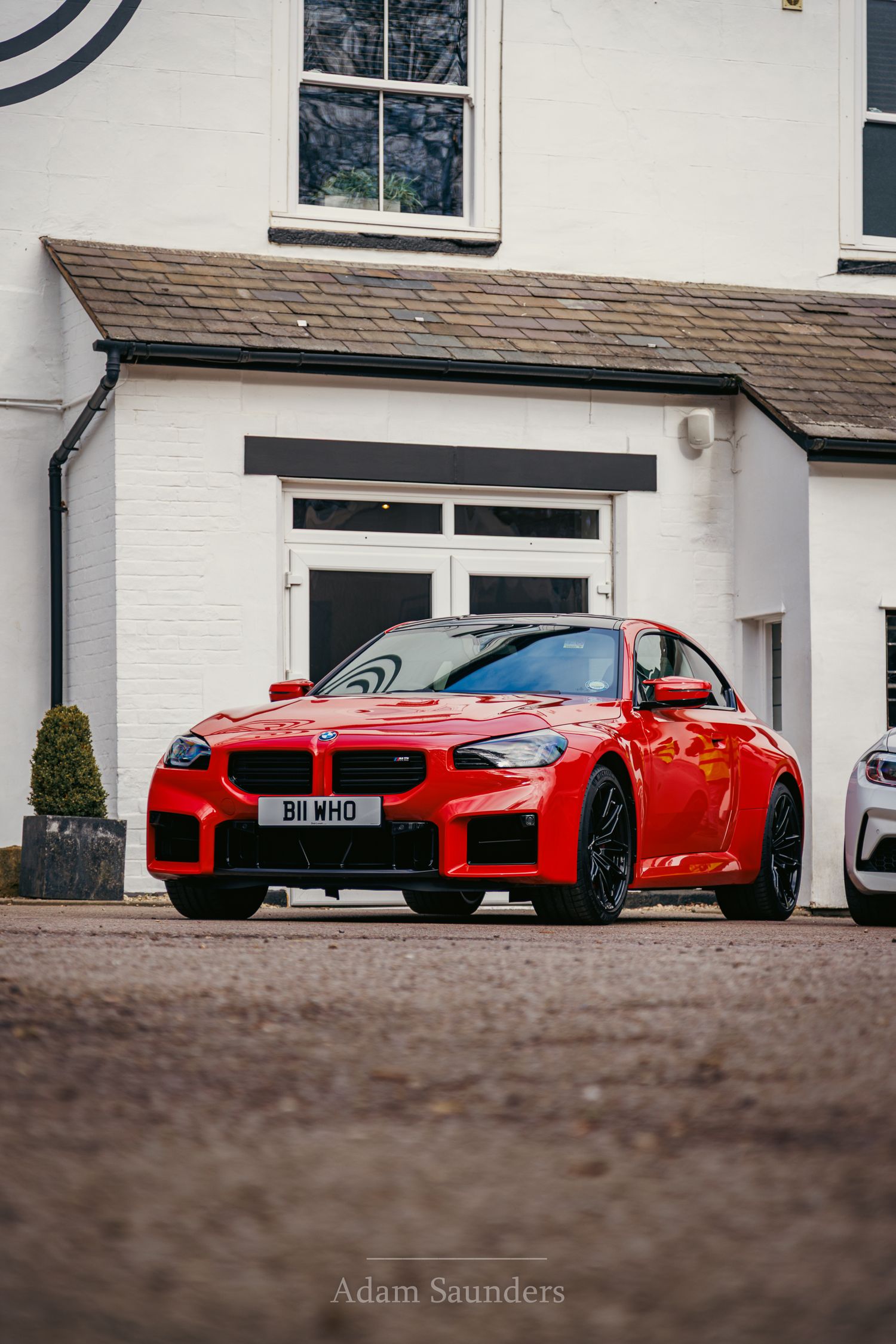 A bright red BMW M performance car with black accents parked in front of a white residential building.