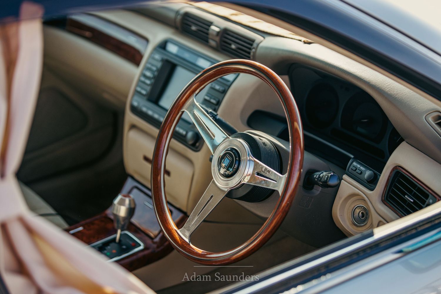 Interior of a luxury car with wooden steering wheel, beige dashboard, and modern center console.
