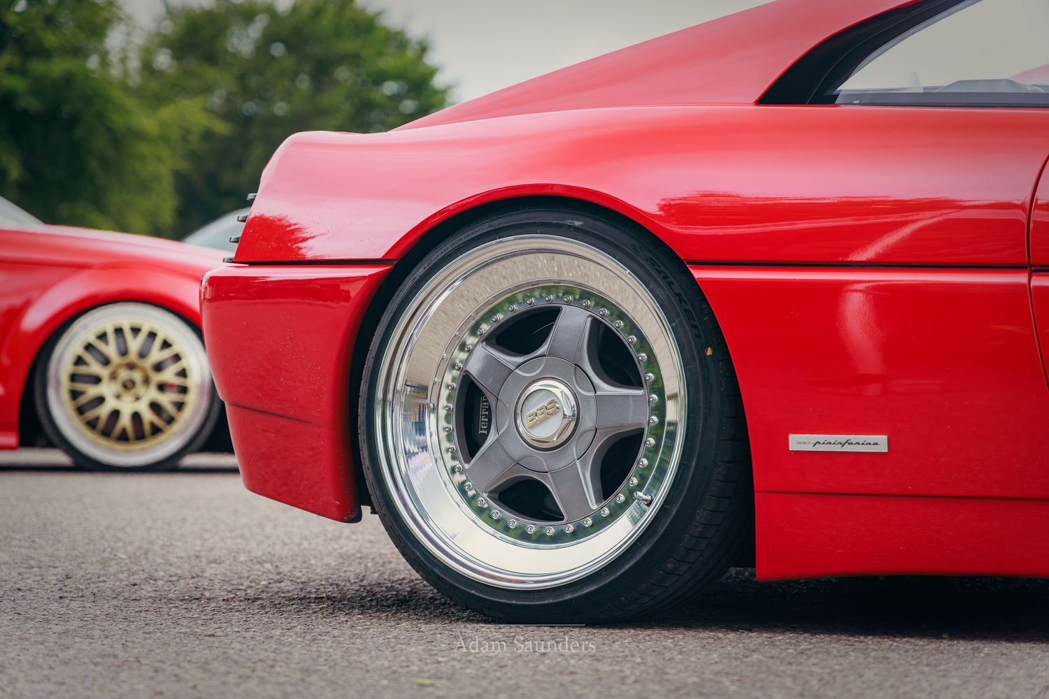Red sports car with polished chrome multi-spoke wheels parked at a car show on asphalt.
