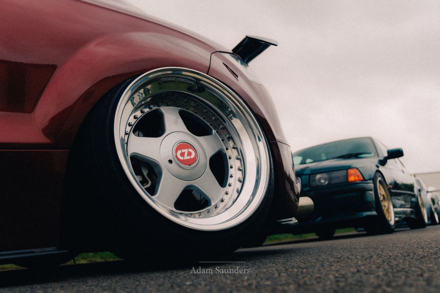 Close-up of a chrome multi-spoke aftermarket wheel on a lowered red car at a car show.
