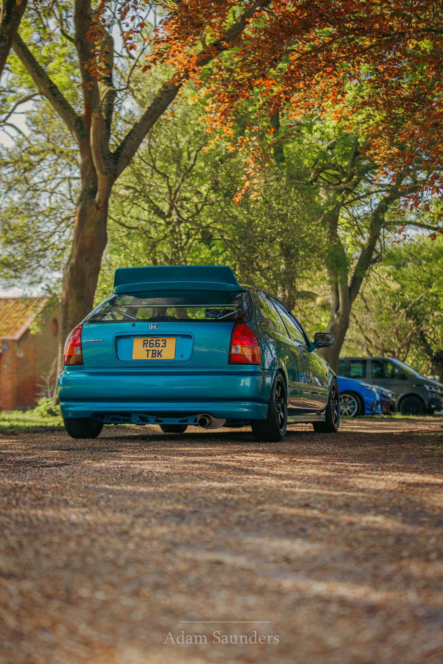 Modified blue Honda Civic parked under autumn trees with golden leaves in a scenic outdoor setting.