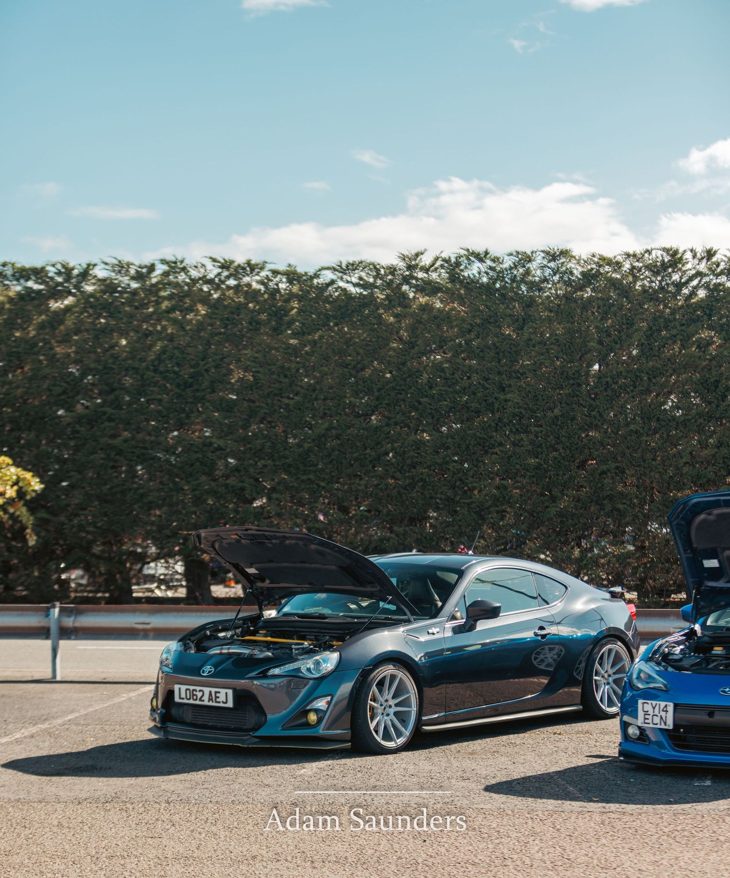A custom black sports car with blue accents and custom wheels is parked next to other performance vehicles.