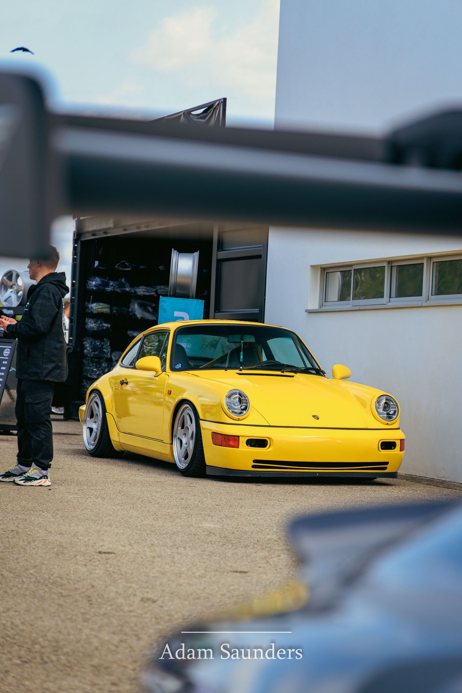 A bright yellow Porsche 911 sports car parked outside a building at a car meet event.