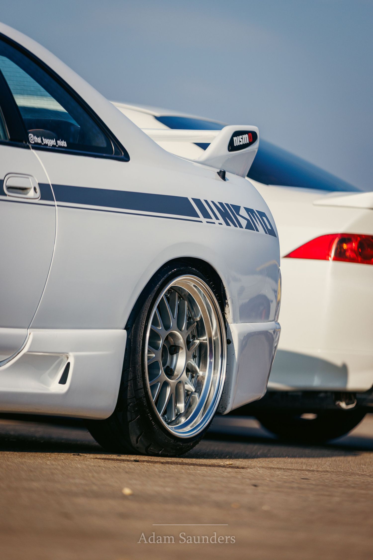 Close-up view of a white sports car's rear quarter panel showing custom silver alloy wheels and lowered suspension.
