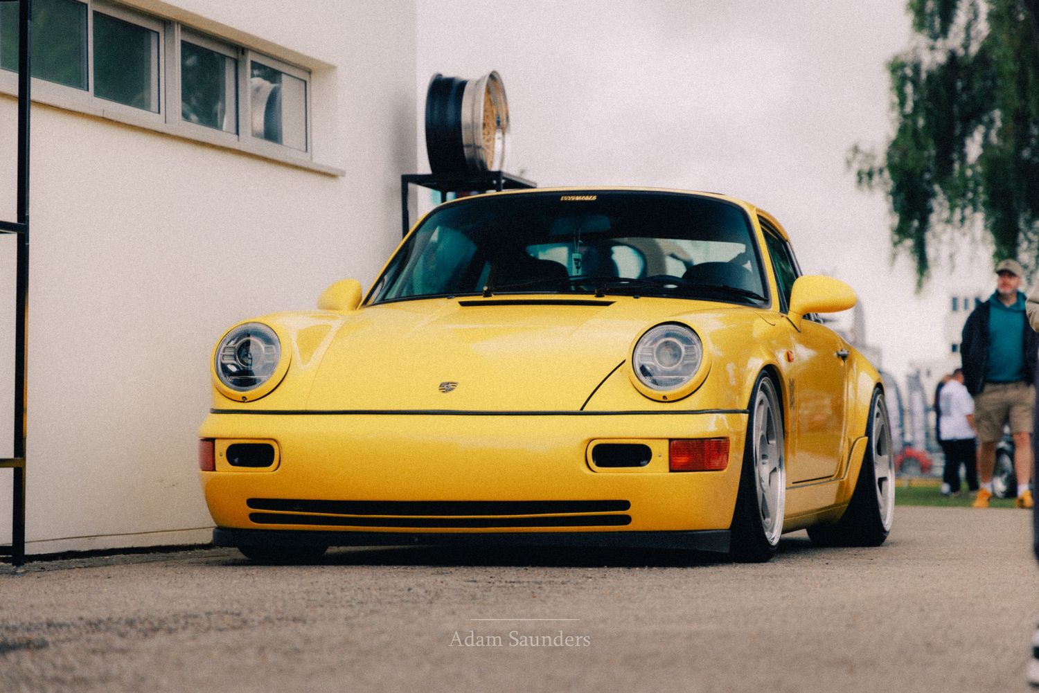 Yellow Porsche 911 sports car parked outdoors, showcasing classic design with round headlights and lowered stance.