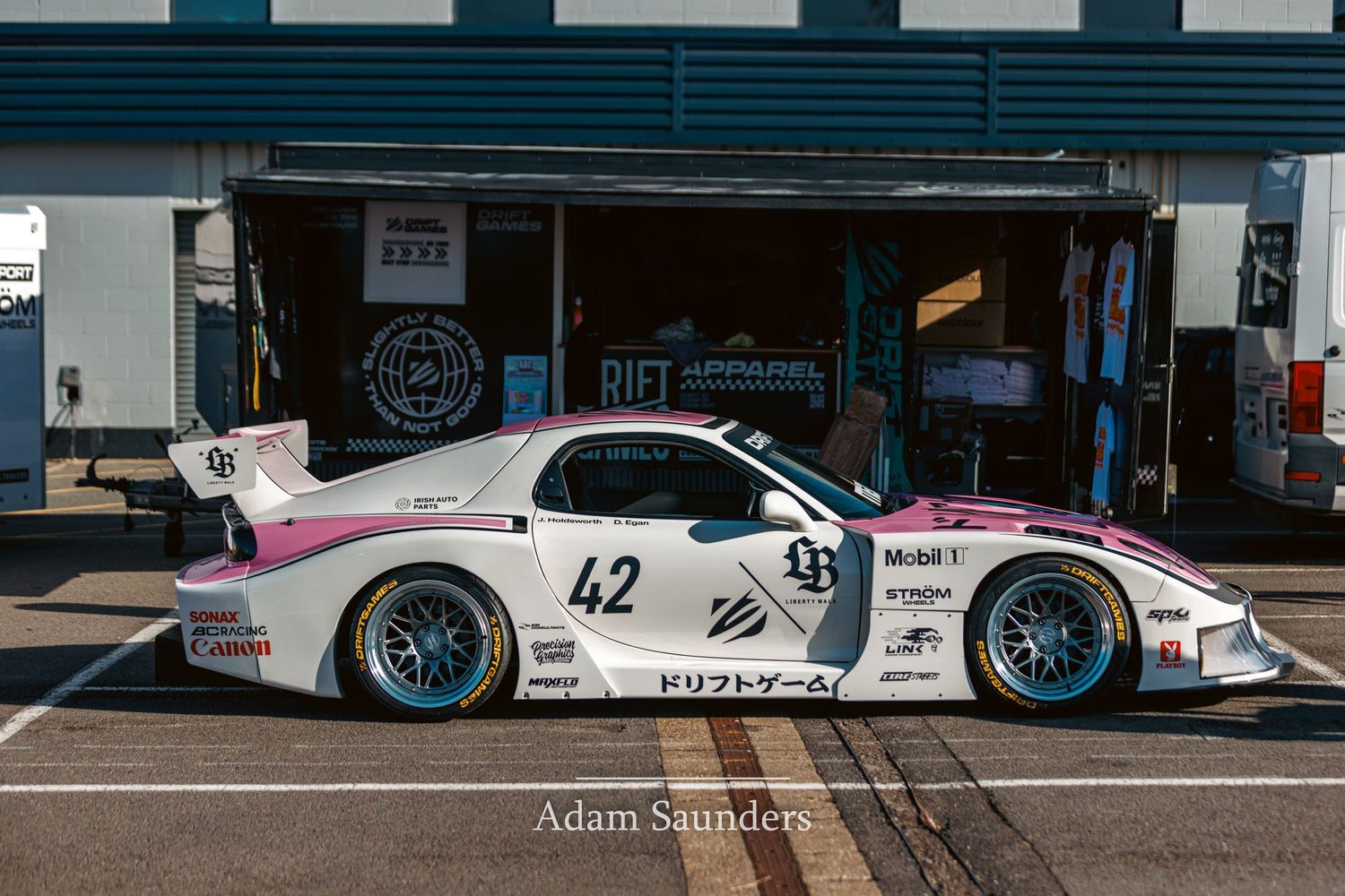 A line of motorsport race cars parked in pit lane with light blue, white and pink JGTC and Le Mans liveries.