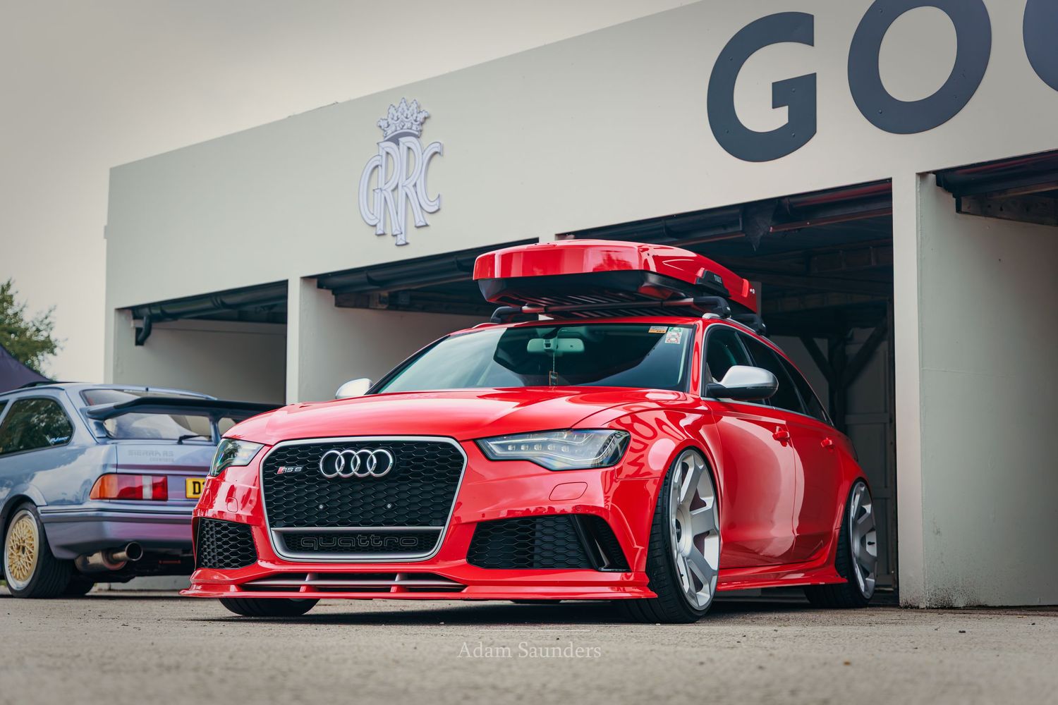 Red Audi RS6 Avant with roof box, lowered stance, and custom wheels parked outside a garage.