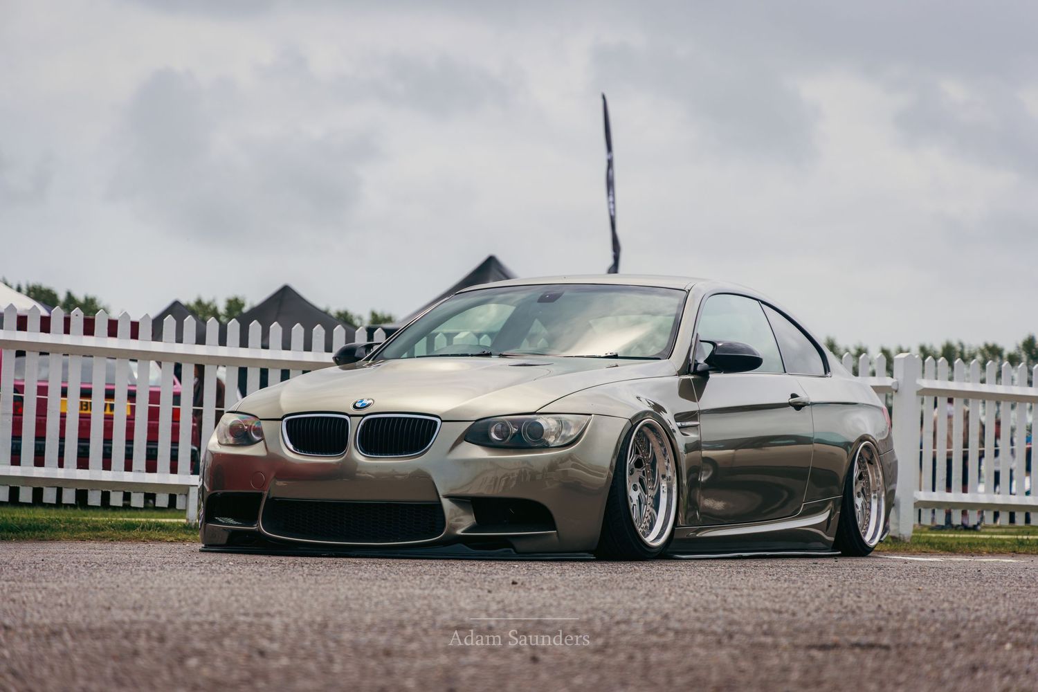 Modified BMW M3 coupe in gold with aggressive stance, wide body kit, and low suspension on a track.