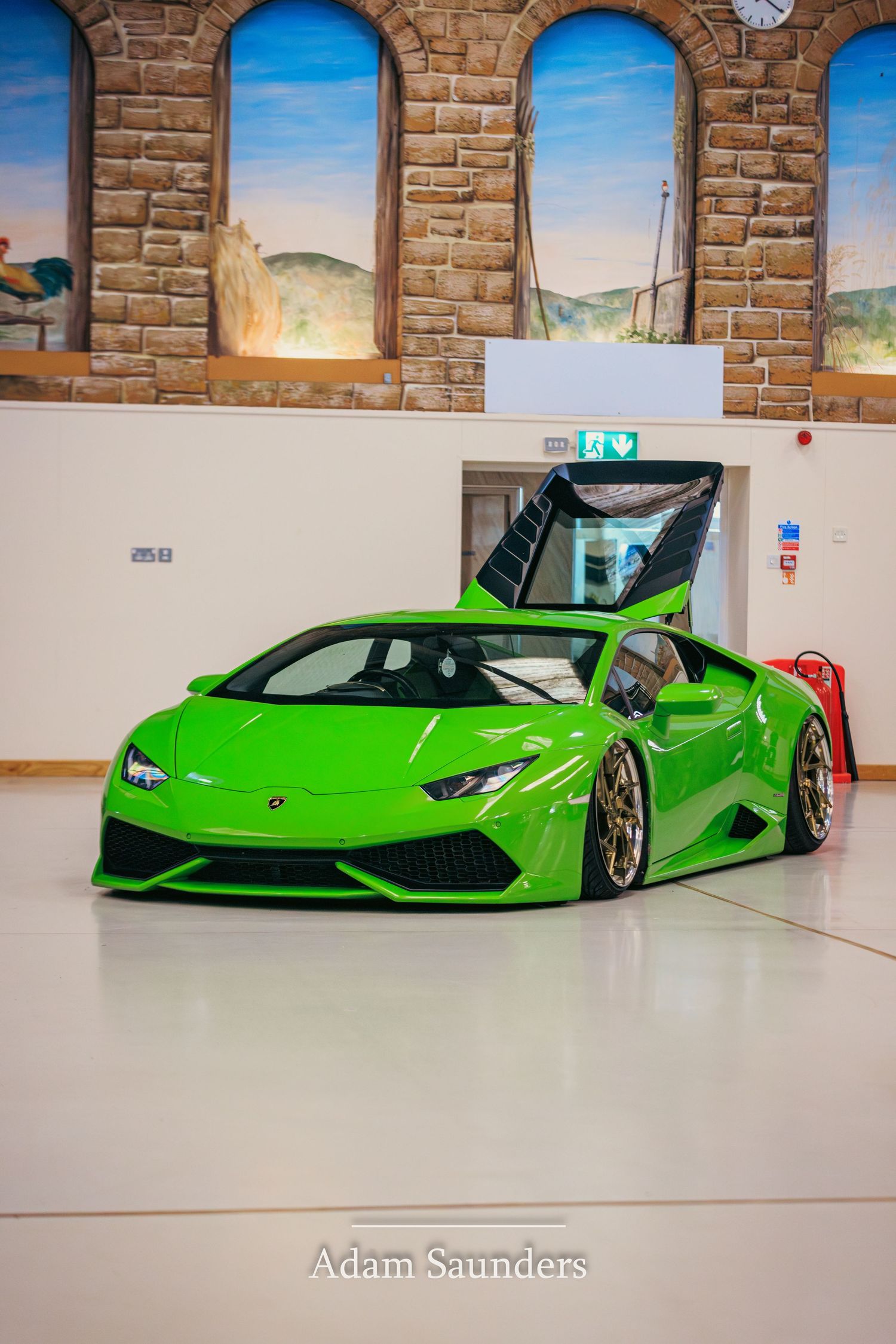 A bright green Lamborghini Huracan supercar with custom lowered suspension sits inside a room with arched stone windows.