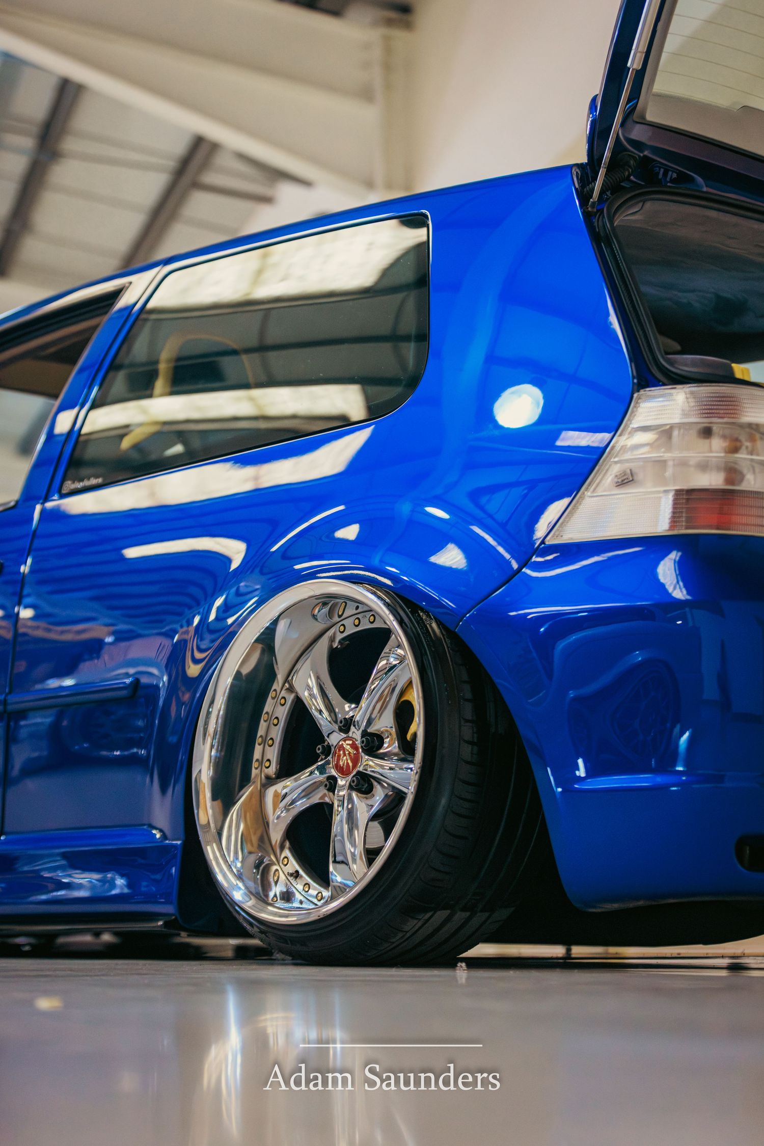 Close-up of a lowered bright blue Volkswagen Golf with custom chrome wheels and aggressive negative camber stance.