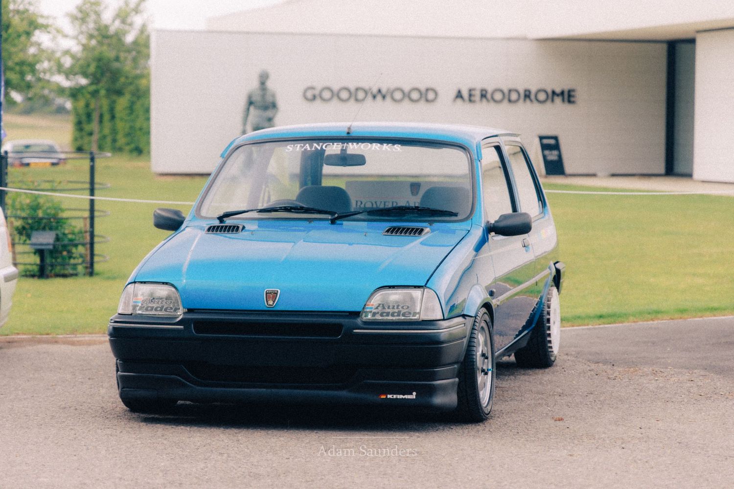 A modified blue Fiat Cinquecento on lowered suspension parked outside Goodwood Aerodrome on a sunny day.
