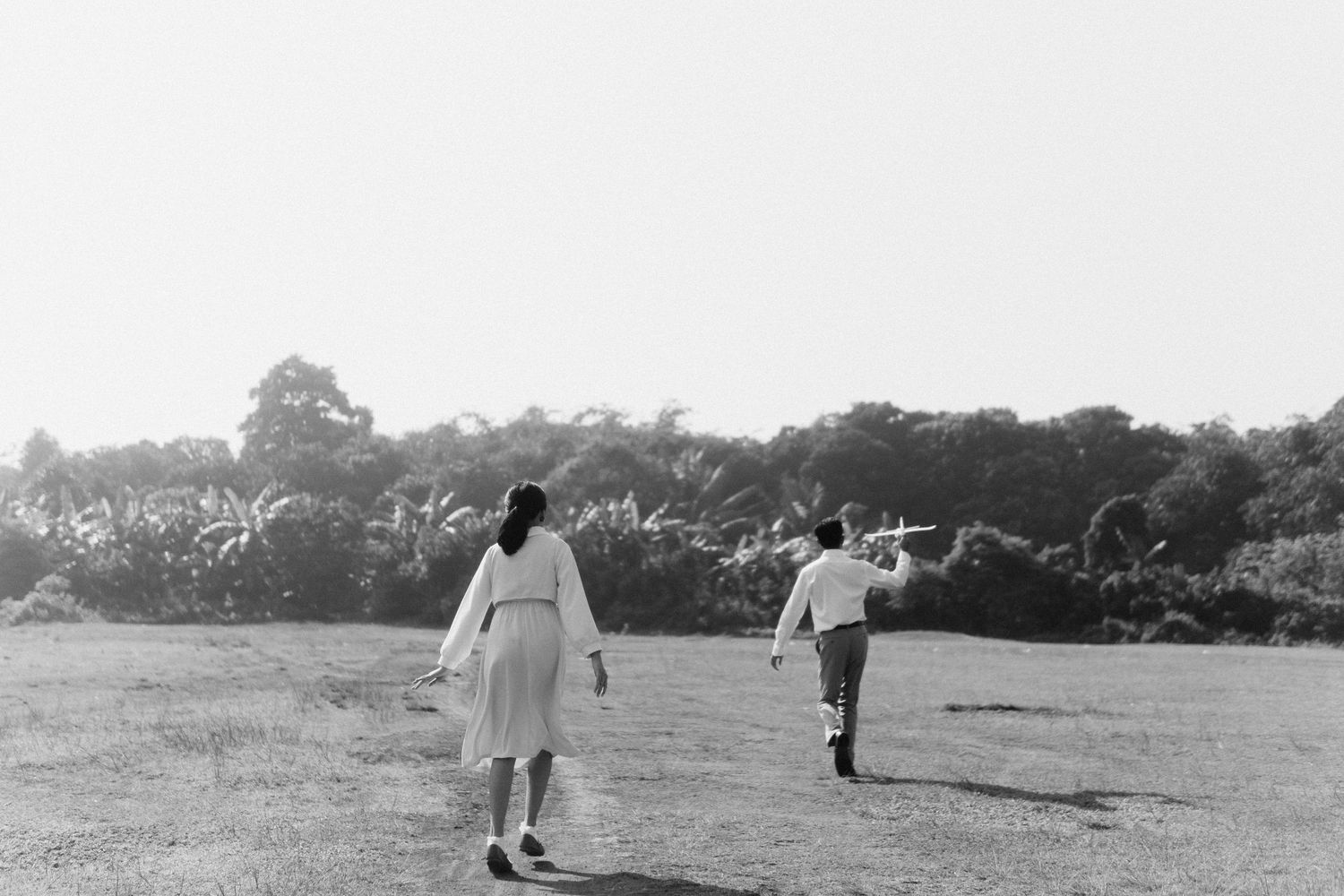 Ghibli inspired photoshoot, the wind rises. The bride and groom running down on a field, black and white photo