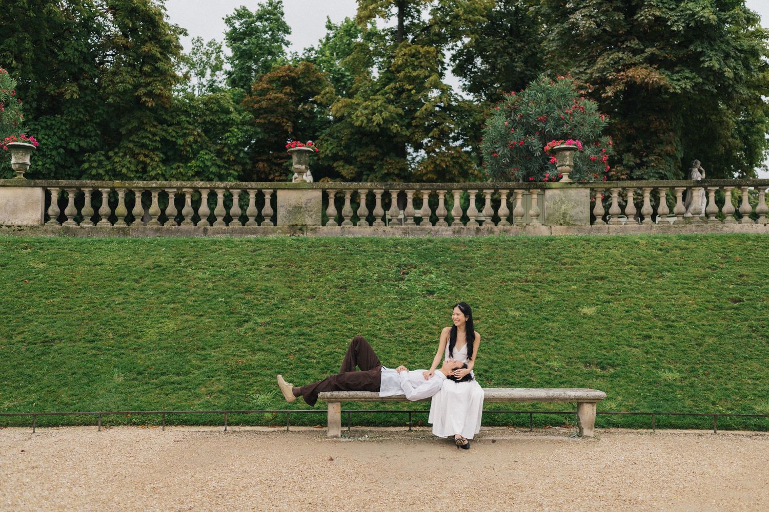 Couple photoshoot at luxembourg garden Paris, the girl is sitting down on a bench while the boyfriend is laying down on her lap