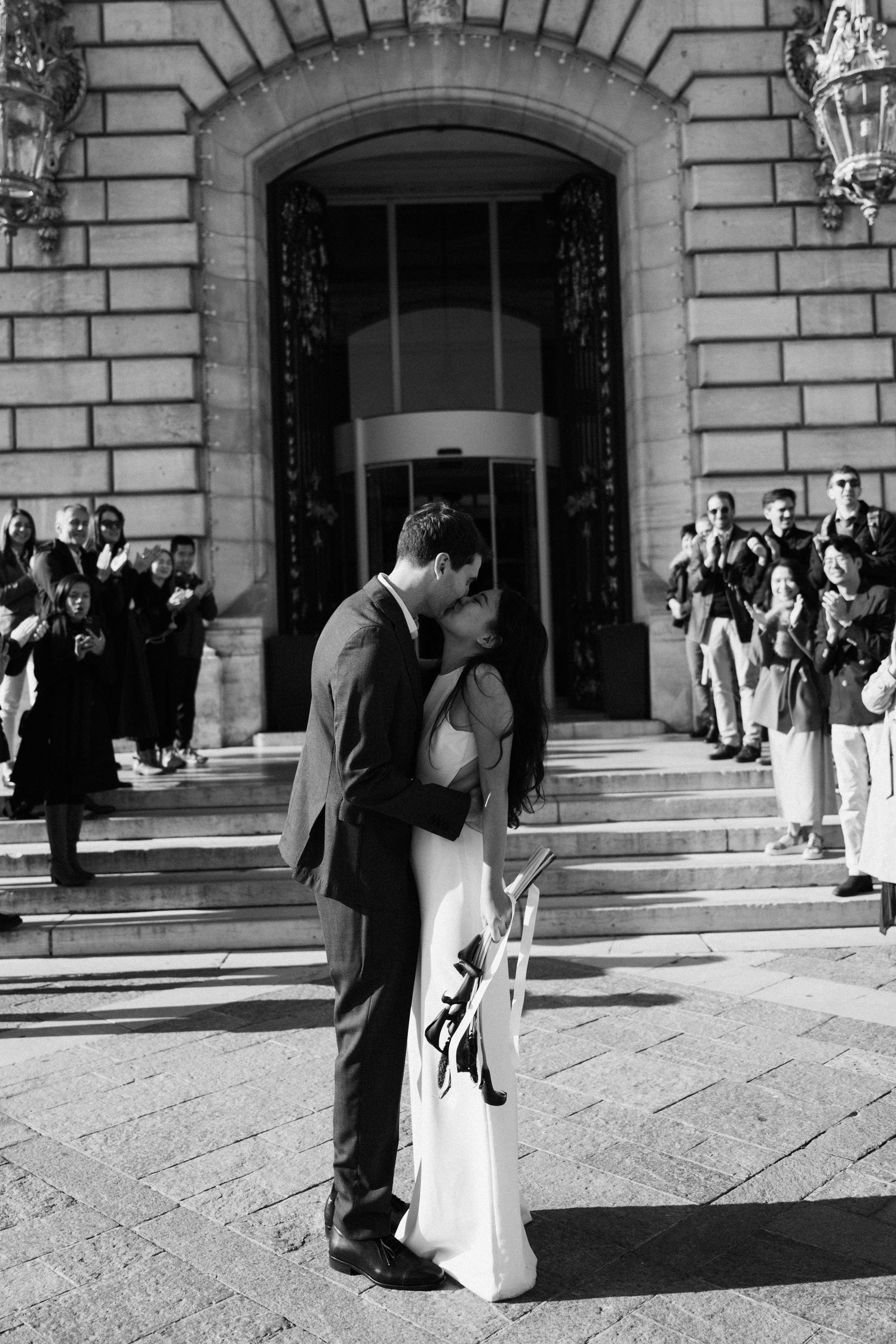 Civil wedding ceremony at Mairie de Levallois-Perret, wedding exit, bride and groom kiss in fron of the building while their friends cheer