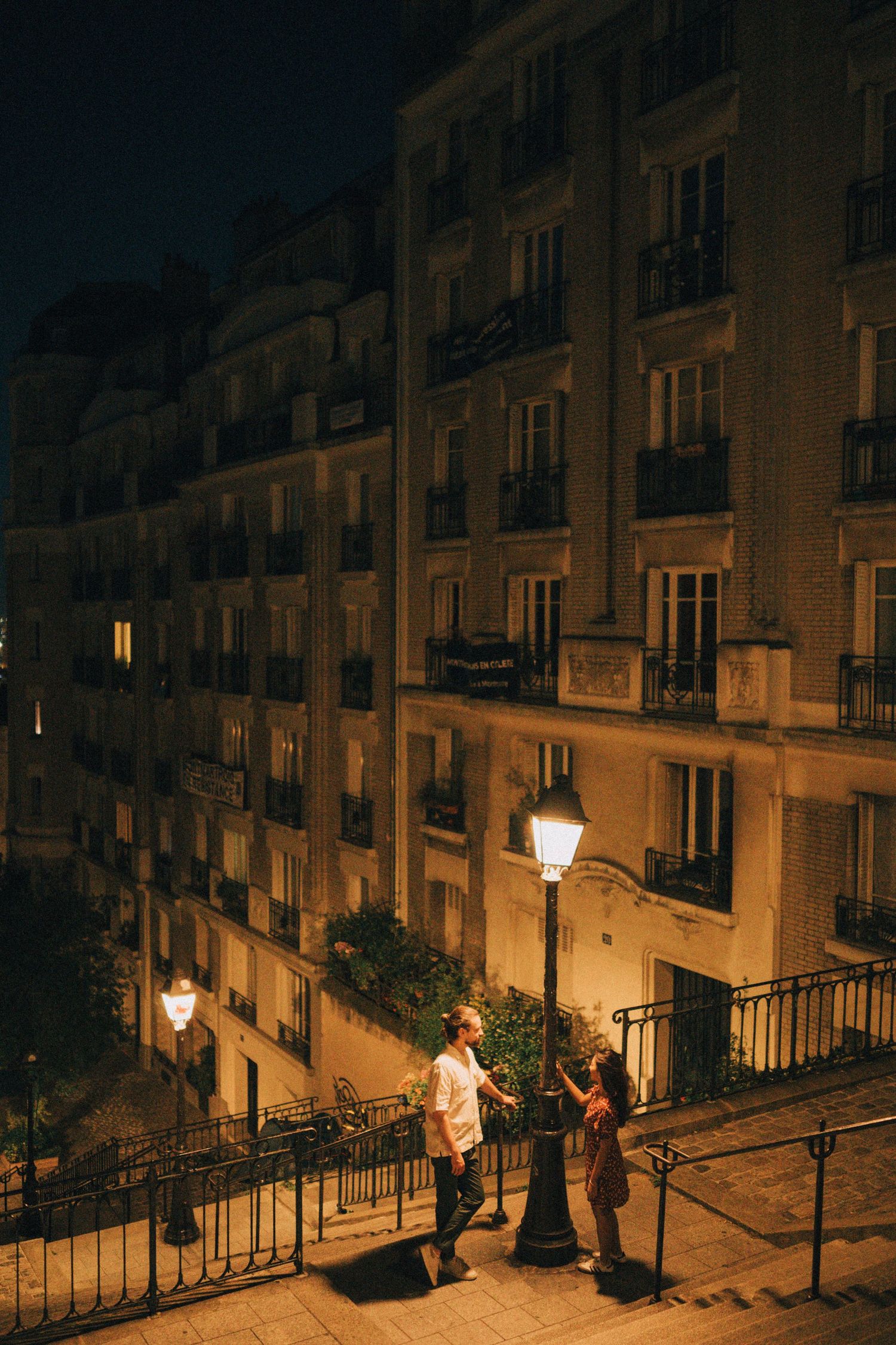 Cinematic night photoshoot in montmartre paris, the couple is standing near a lamp post