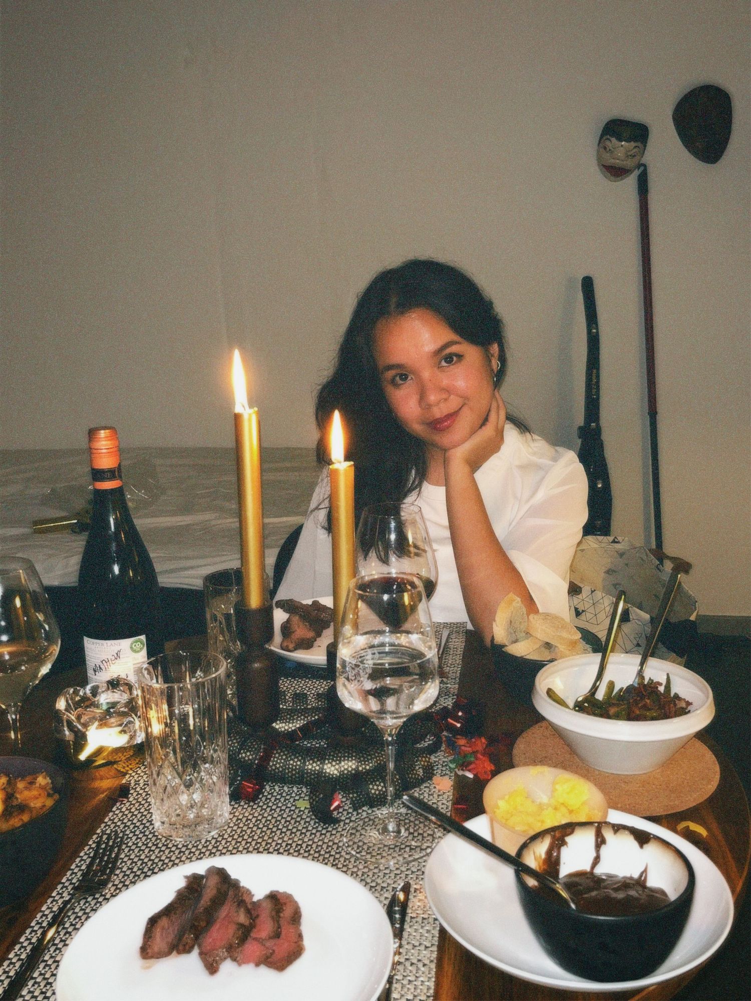 A girl sitting down on dinner table with candles and food, looking and smiling at the camera, christmas dinner aesthetic