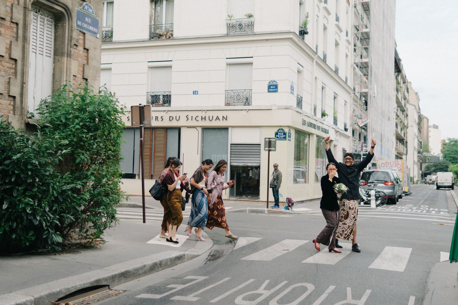 Bride and groom walking on Paris street wearing Indonesian traditional costume, with their friends behind them