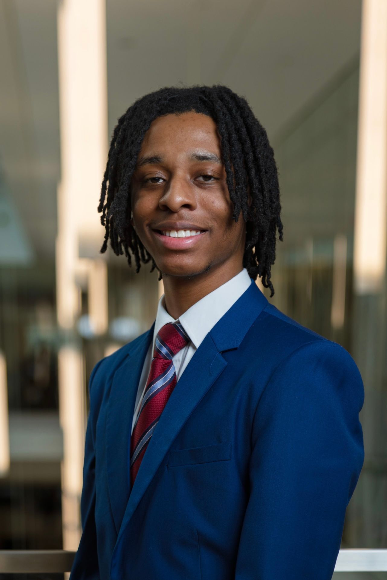Professional portrait of person in navy suit and striped tie with dreadlocks hairstyle.