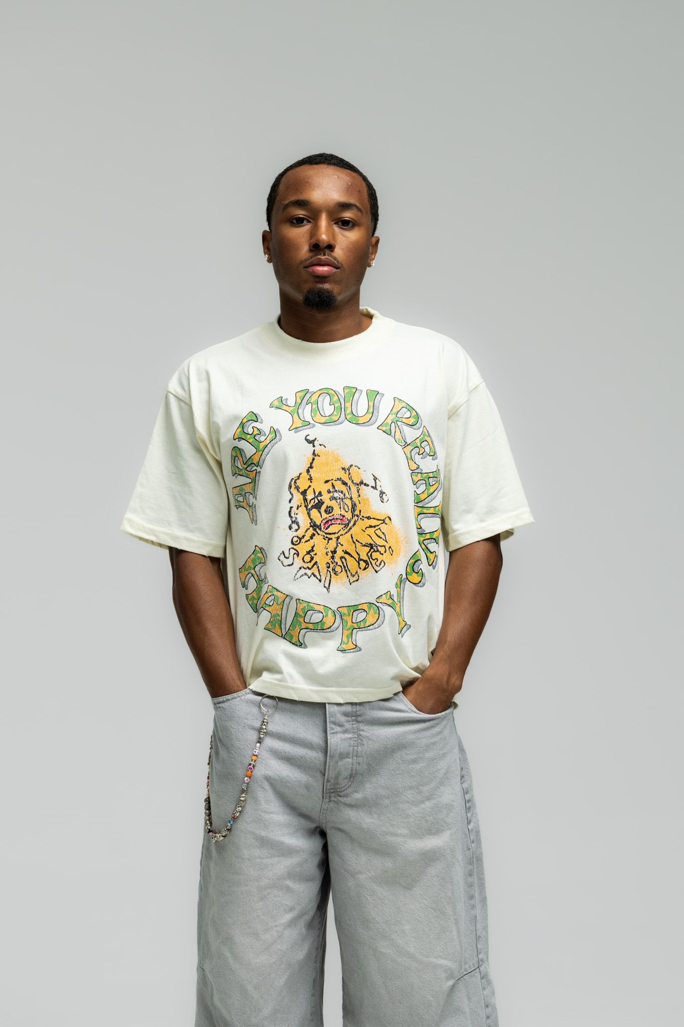 Person wearing a white graphic t-shirt with colorful print and light gray pants against a white background.