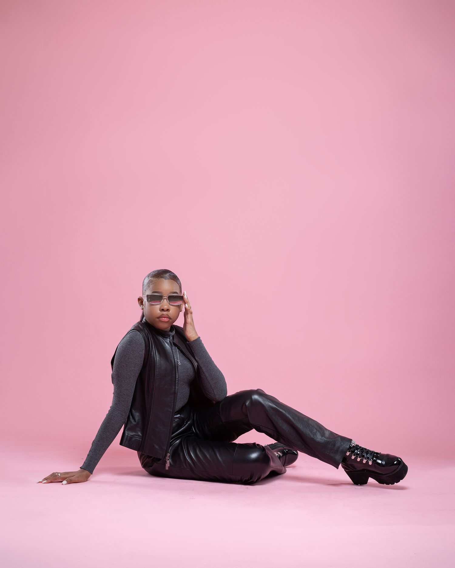 Modern fashion portrait of someone in black leather outfit posing against pink backdrop with confident style and attitude.