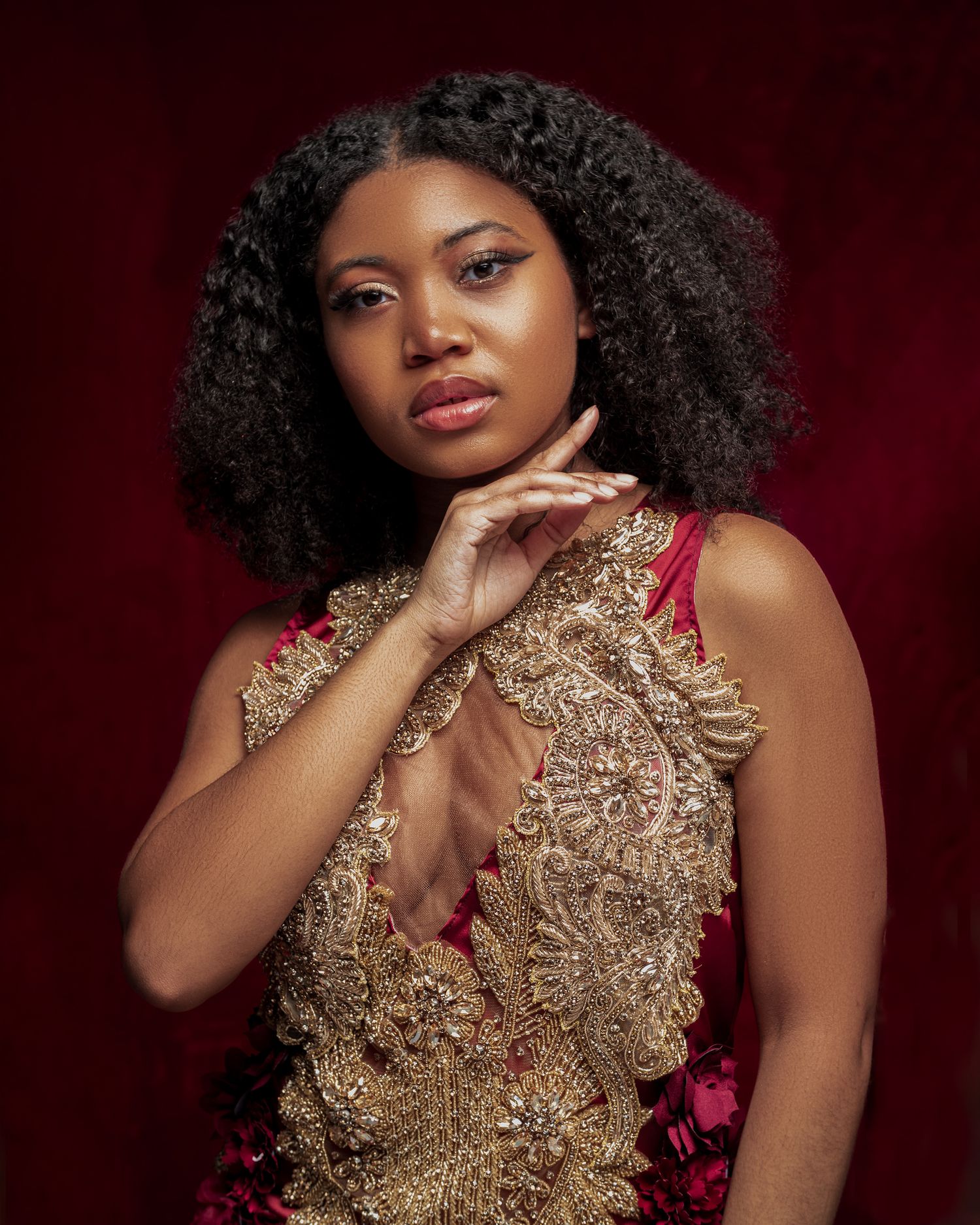 Elegant beauty portrait against dark red background wearing an intricate gold embellished gown.