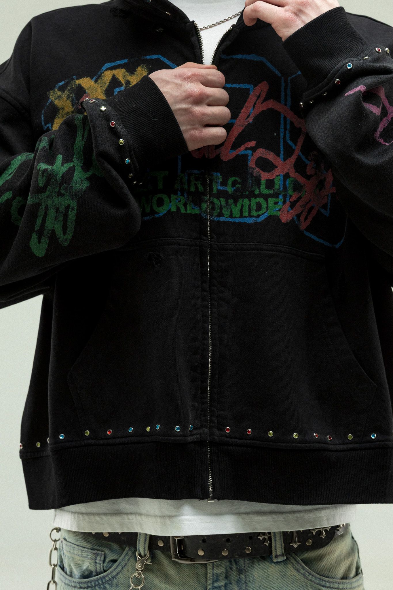 Close-up view of black denim jacket with colorful graffiti-style artwork and metal studs along the bottom edge.