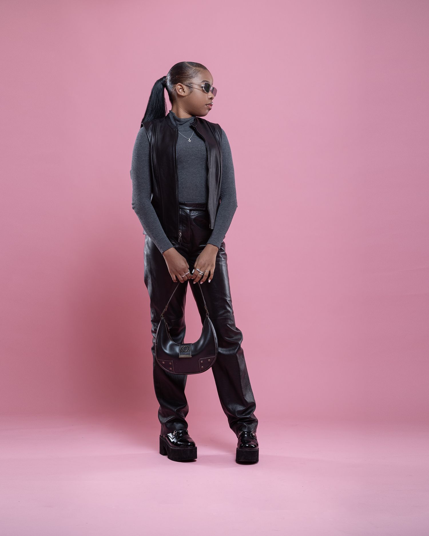 Person in casual streetwear outfit with black jacket and pants poses against pink studio background.