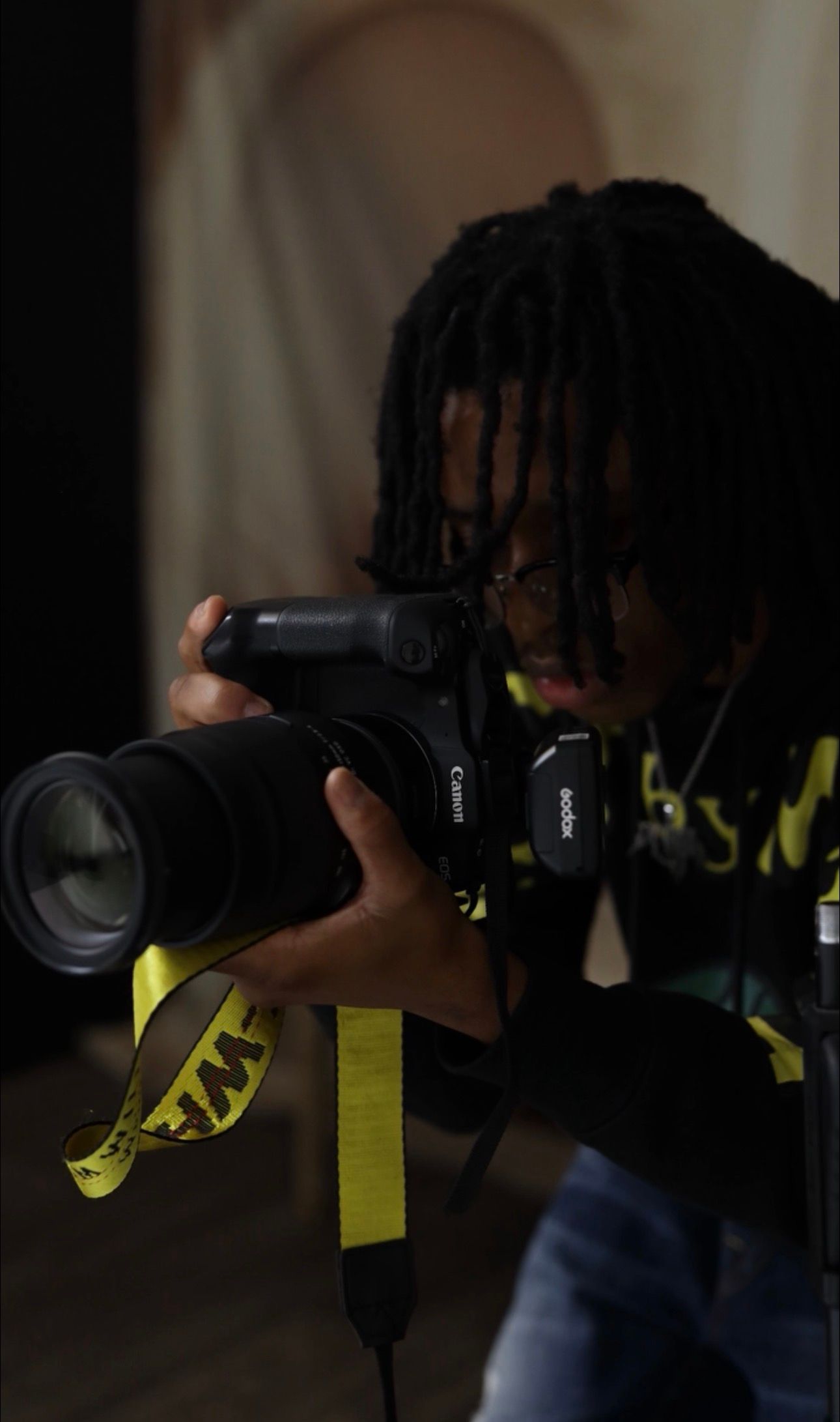 A photographer holds a professional camera with a telephoto lens against a dark background.