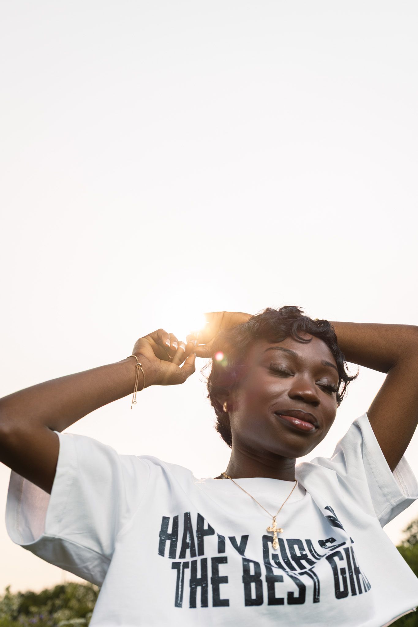 A person wearing a white t-shirt with text poses against a bright sunlit sky in a serene outdoor setting.