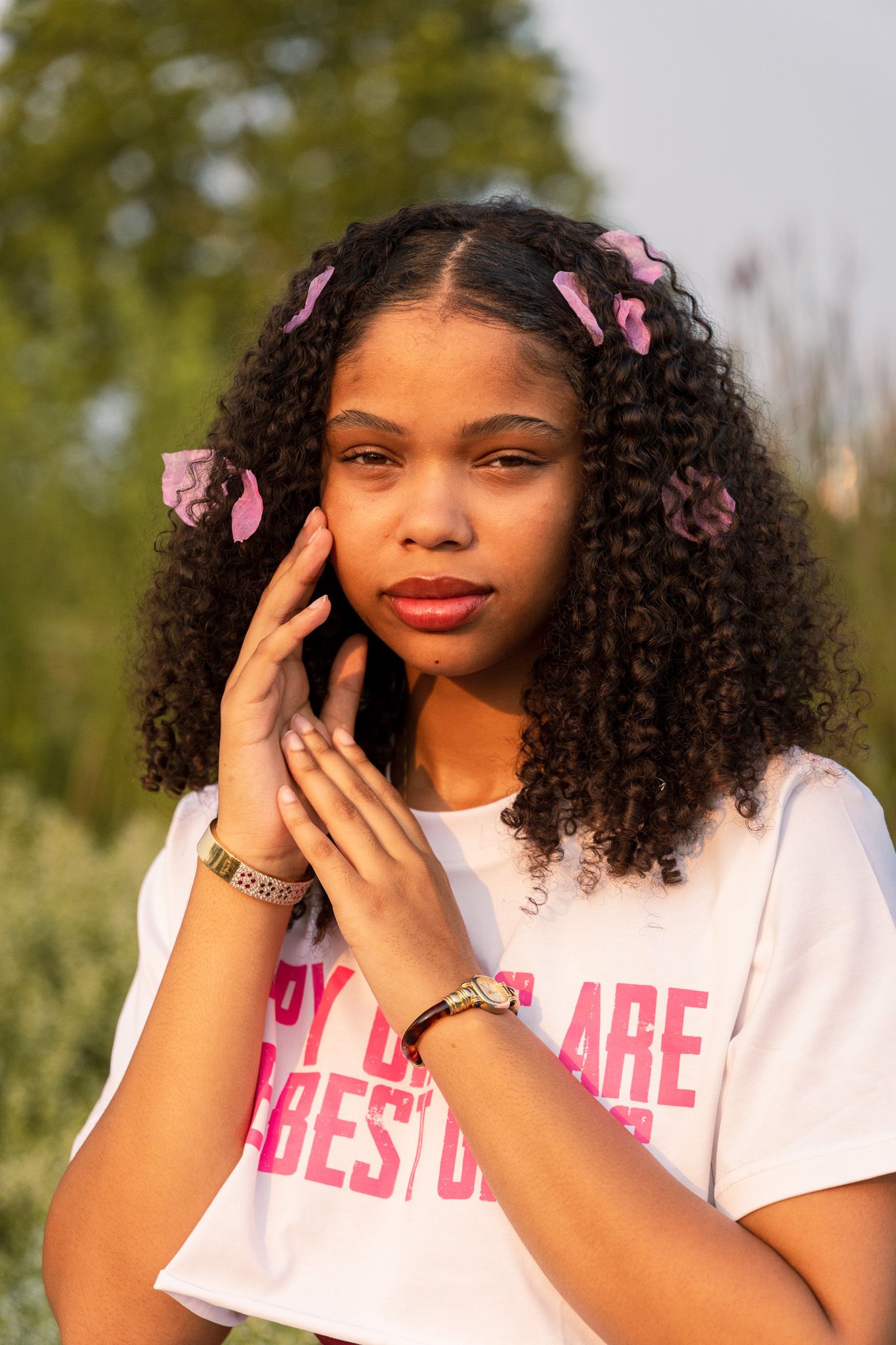 A series of outdoor portrait photos showing someone wearing a pink shirt with hair accessories in golden sunlight.