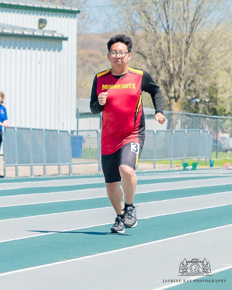 Runner in red athletic wear sprinting on a green track during training or competition.