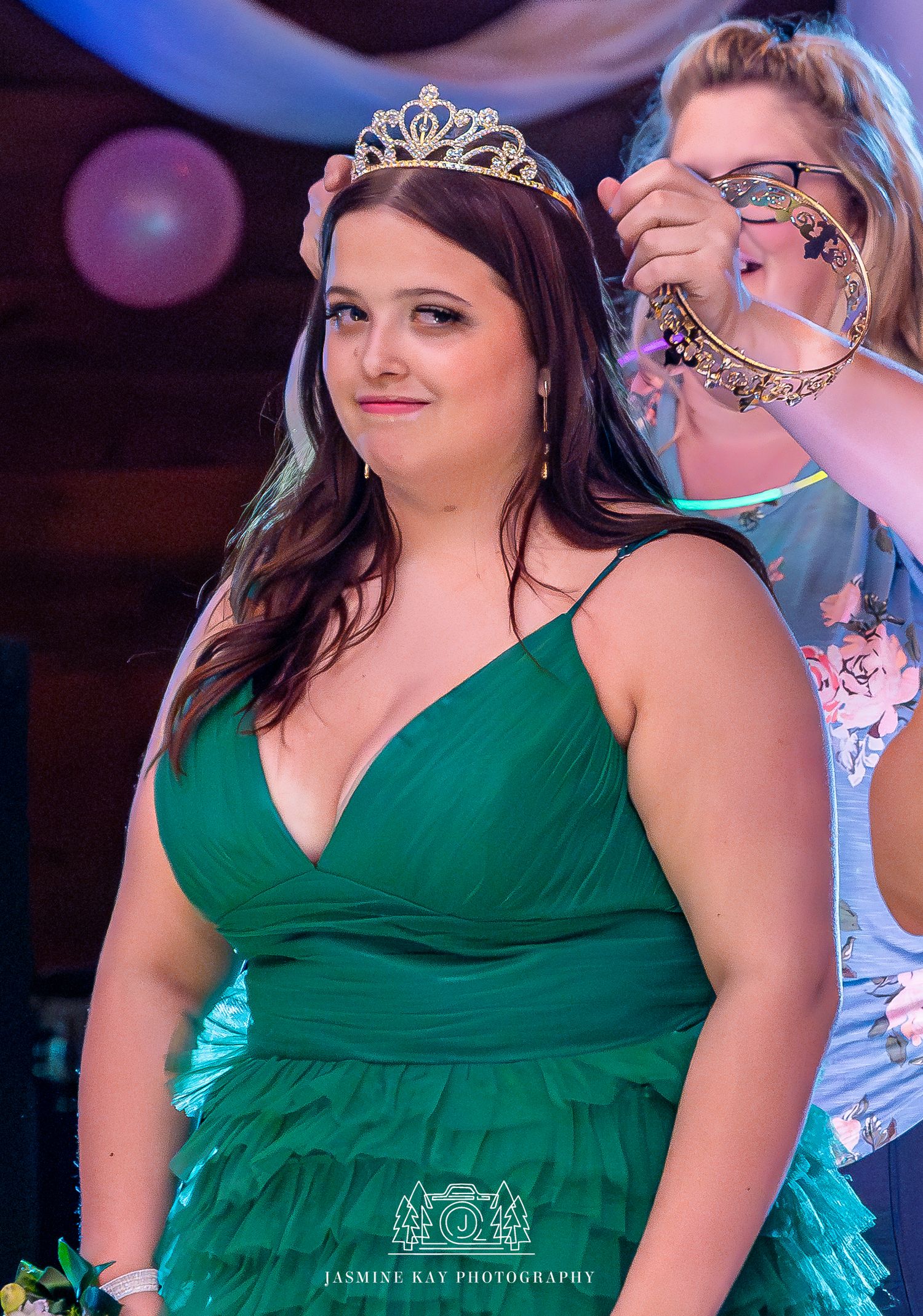 A woman in an emerald green formal dress poses during a celebration event with blue lighting in the background.