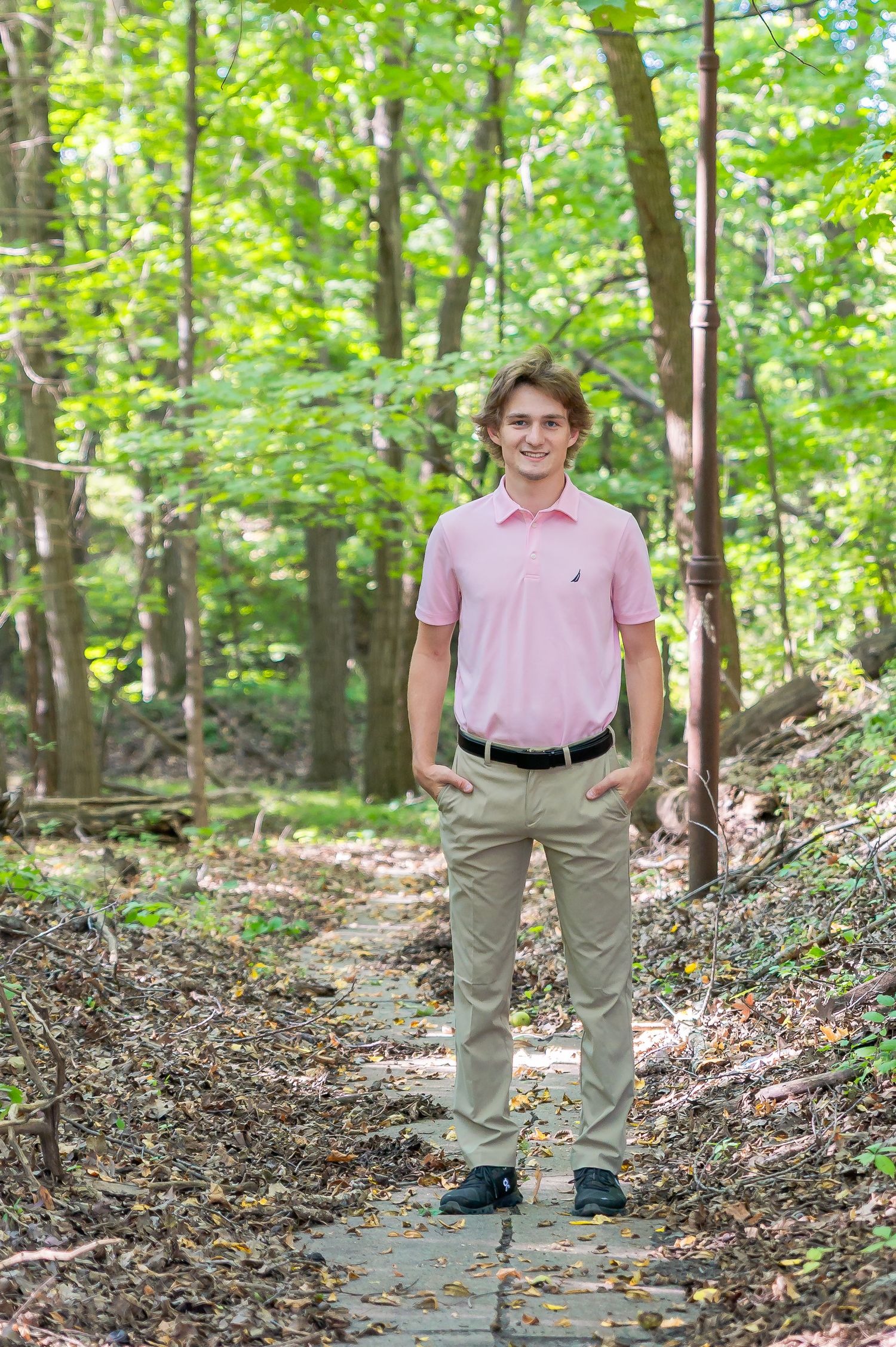 Someone in a pink polo shirt and khaki pants stands on a stone path in a lush green forest setting.
